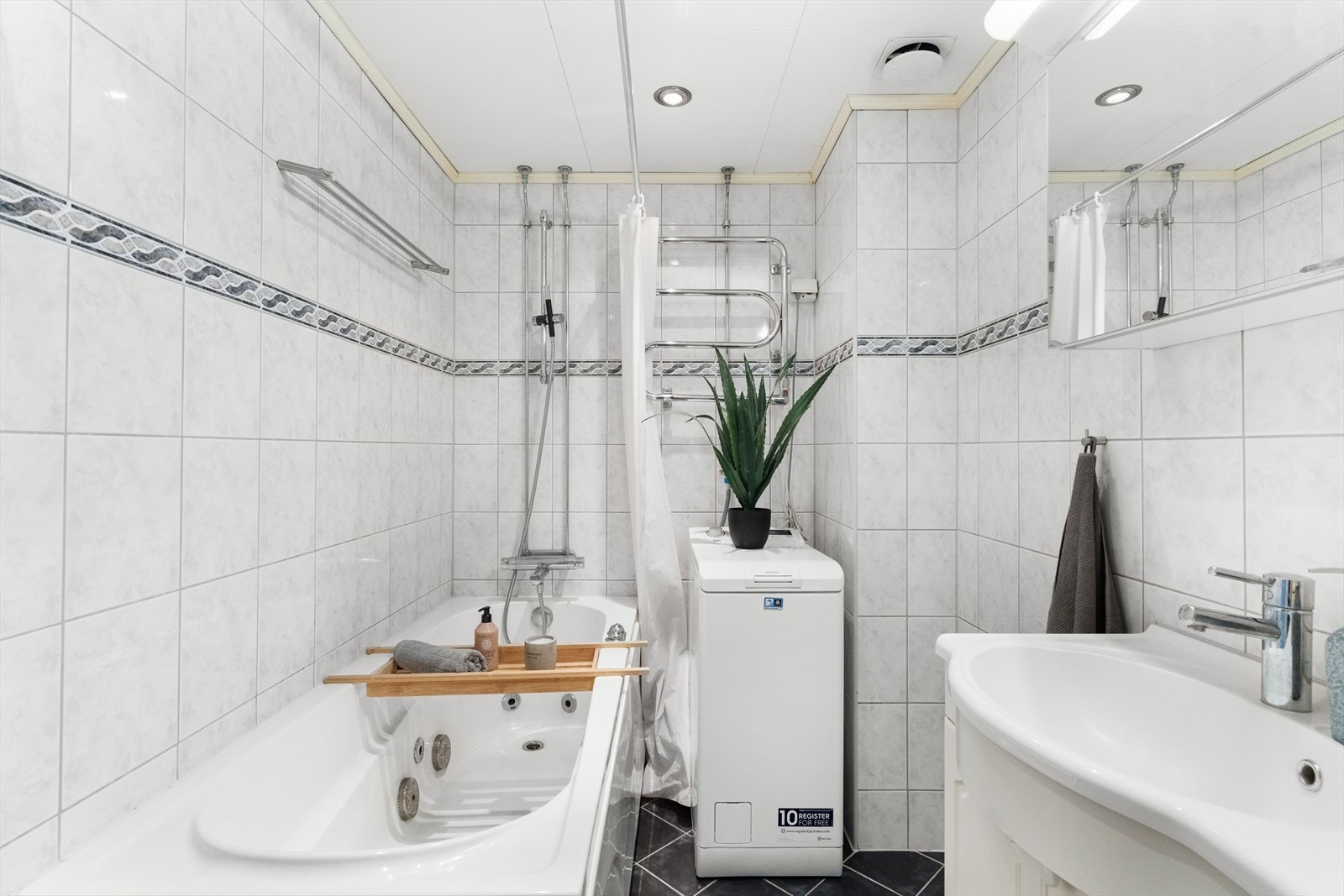 Badet har blant annet badekar, smal vaskemaskin, varmekabler i gulv, vegghengt toalett og servant med innredning Galleribilde