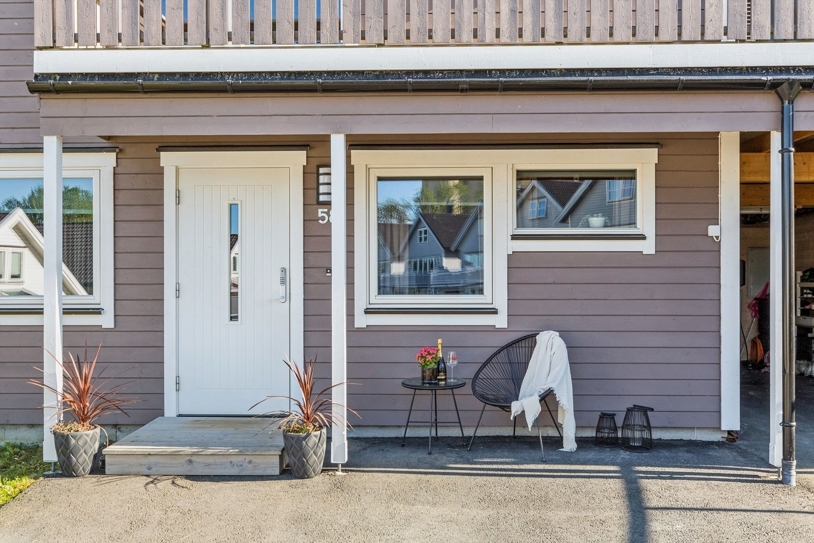 I forkant av boligen er det en asfaltert gårdsplass, liten plen og inngangsparti skjermet av veranda i etasjen over. Galleribilde