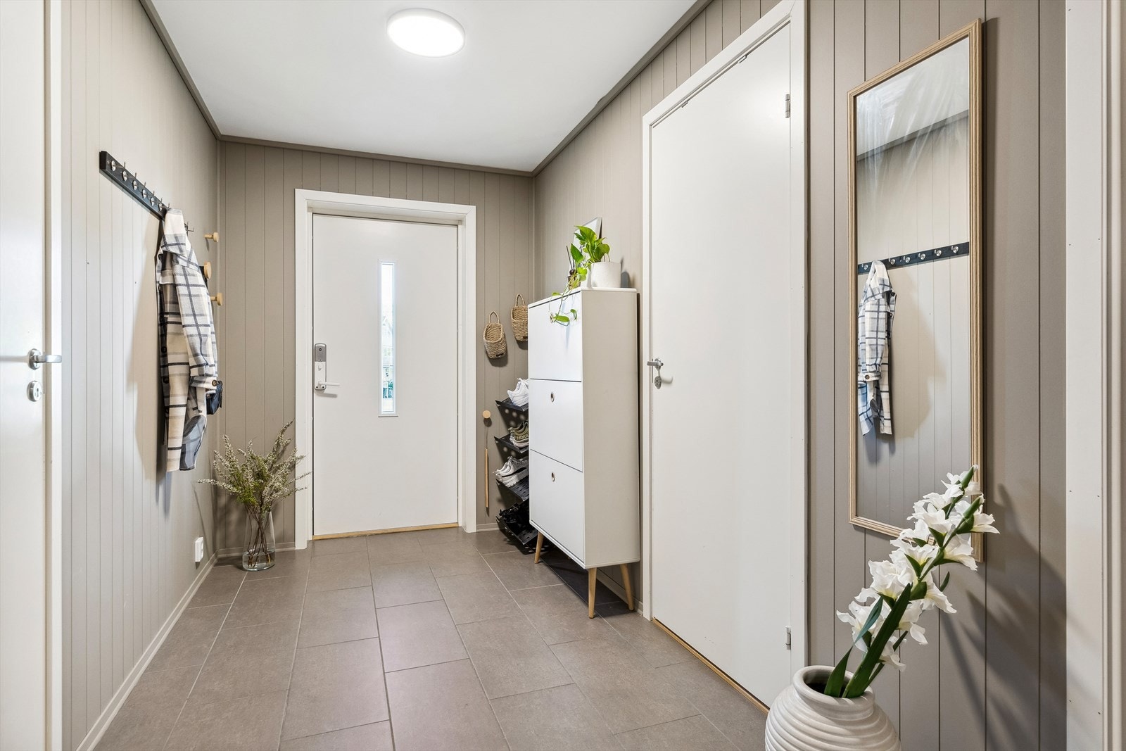 Den hvite inngangsdøren åpner opp til en flott entré med flislagt gulv og veggpanel malt i en rolig, harmonisk farge. Galleribilde