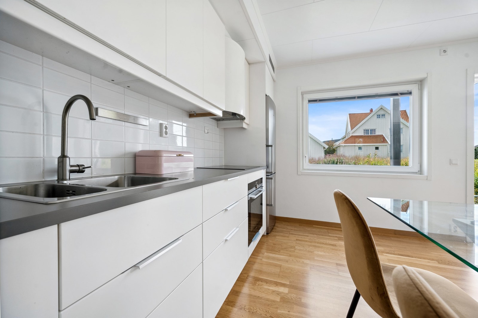 Benkeplater av laminat, nedfelt oppvaskkum med ettgreps armatur, det er flislagt mellom kjøkkenbenk og overskap, benkeskapsbelysning under overskap, integrert komfyr med nedfelt induksjonstopp, og frittstående kjøleskap med frysedel Galleribilde