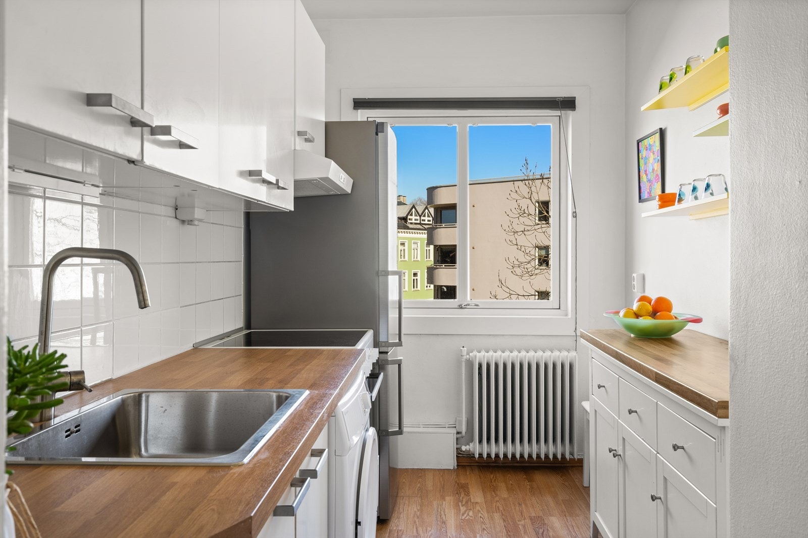 Lyst kjøkken med glatte fronter og laminat benkeplate. Det er montert lys under overskap for ekstra benkebelysning og stikkontakter for bruk av kjøkkenutstyr. Galleribilde