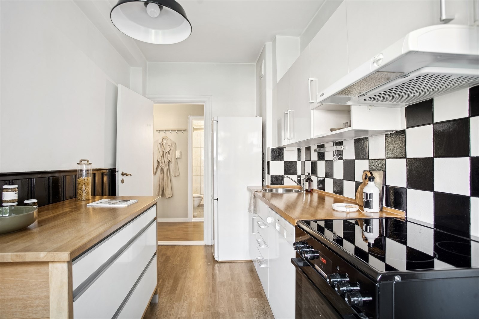 Kjøkkeninnredning med glatte, malte fronter. Heltrebenkeplate med nedfelt kum i rustfritt stål. Fliser på vegg over benk. Galleribilde