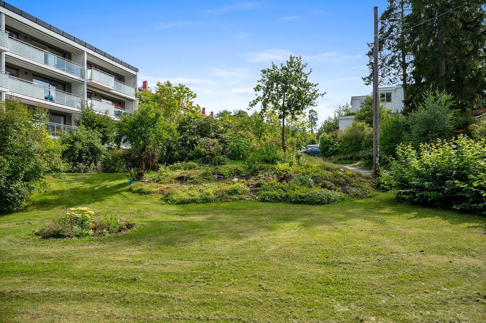 Sameiet har en pent opparbeidet tomt med plen, prydbukser, vei og parkeringsareal. Galleribilde