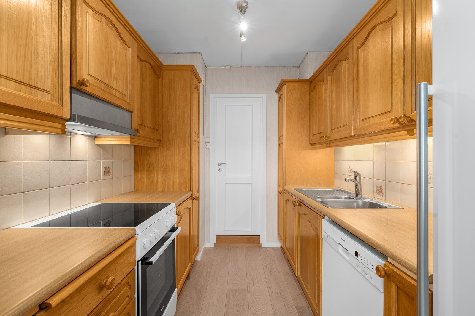 Benkeplaten er av laminat med nedfelt vask og skyllekum. Det er opplegg og plass for oppvaskmaskin og komfyr med glasskeramisk koketopp. Galleribilde