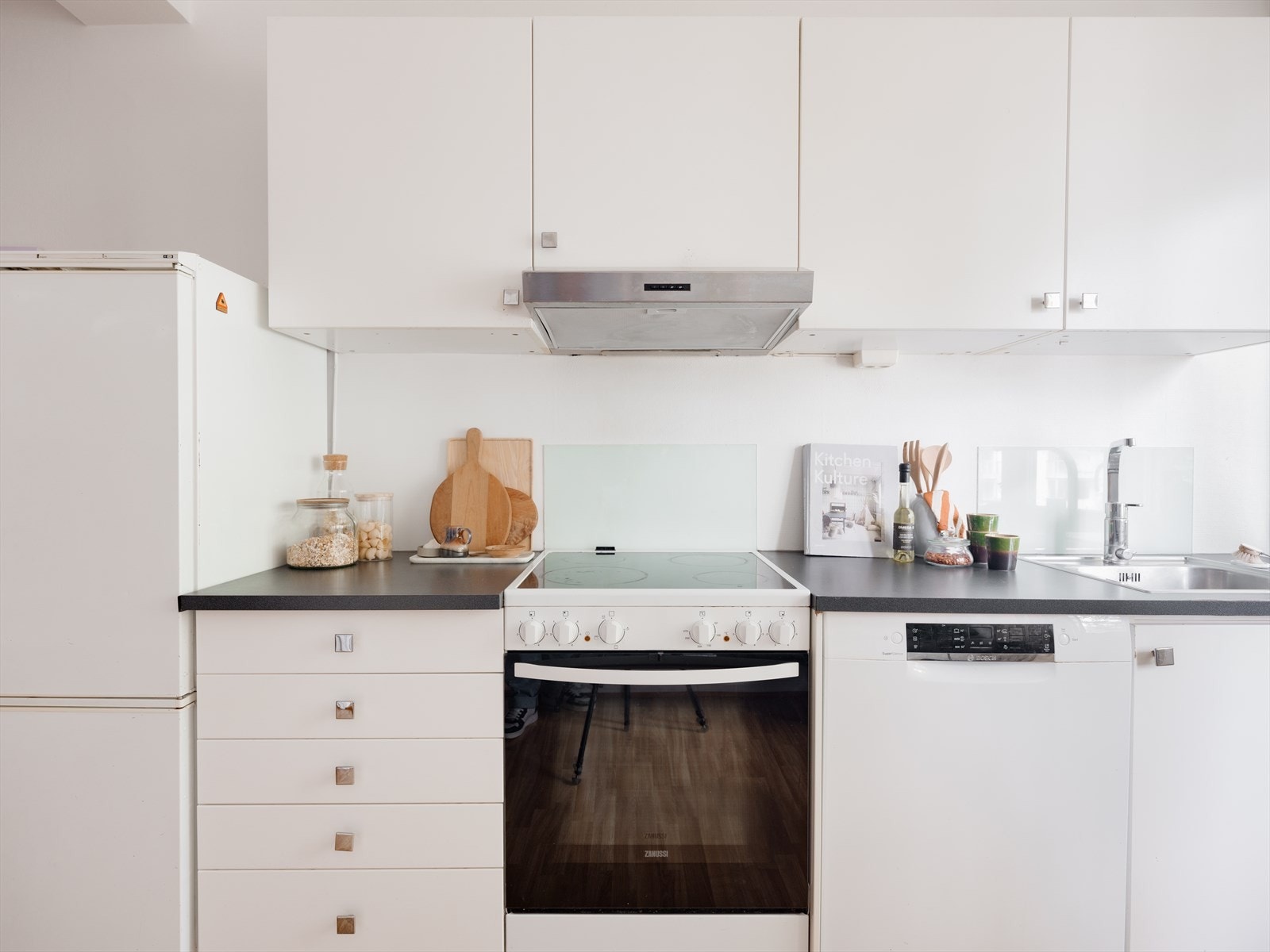 Kjøkkenet har et tidløst og elegant design, bestående av slette, hvite fronter og lys grå benkeplate. Alle hvitevarer medfølger. Galleribilde