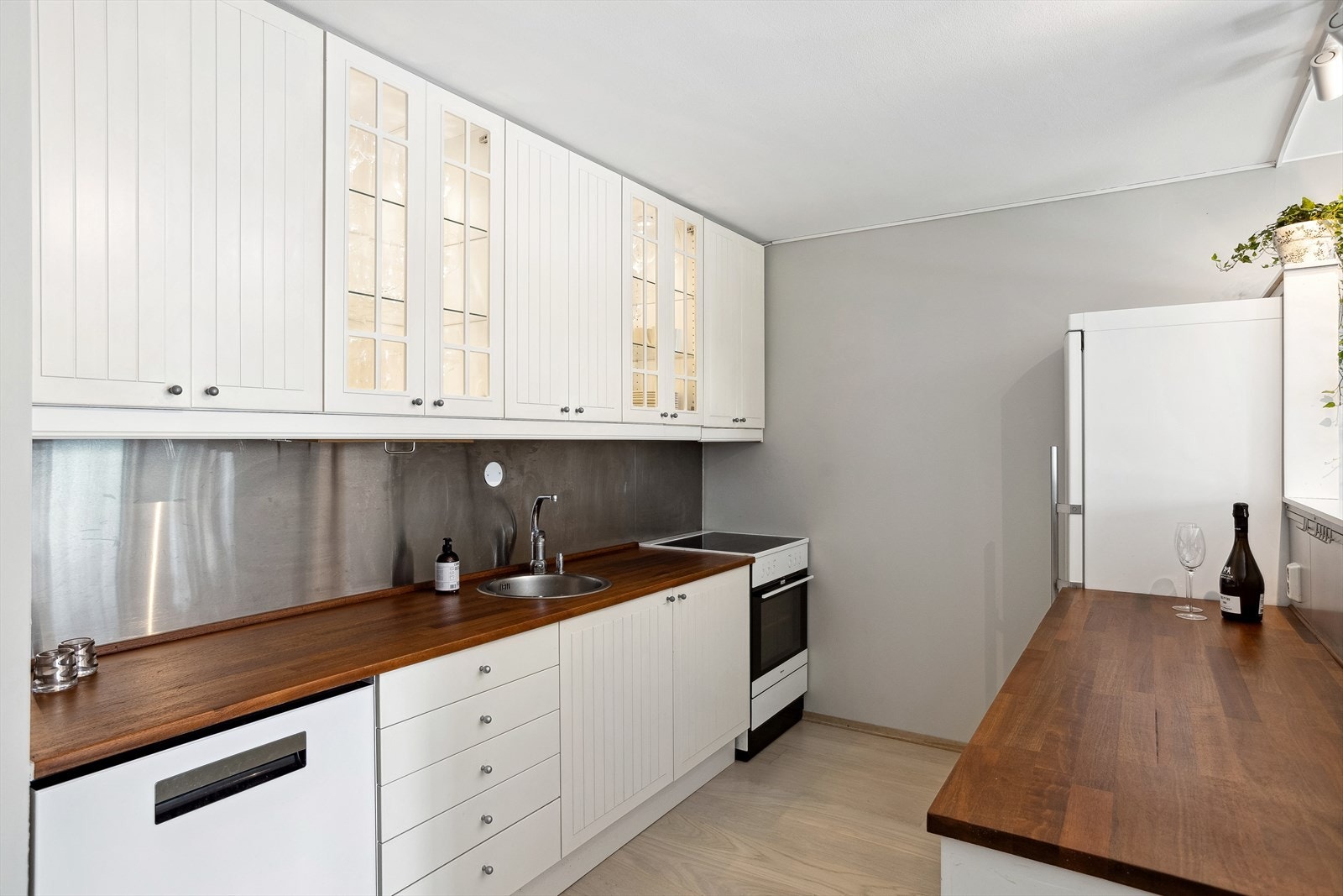 Kjøkkeninnredning med hvite riflete fronter.
Heltre benkeplater med nedfelt kum i rustfritt
stål. Fire glassdører i overskap. Belysning i samme
overskap. Galleribilde