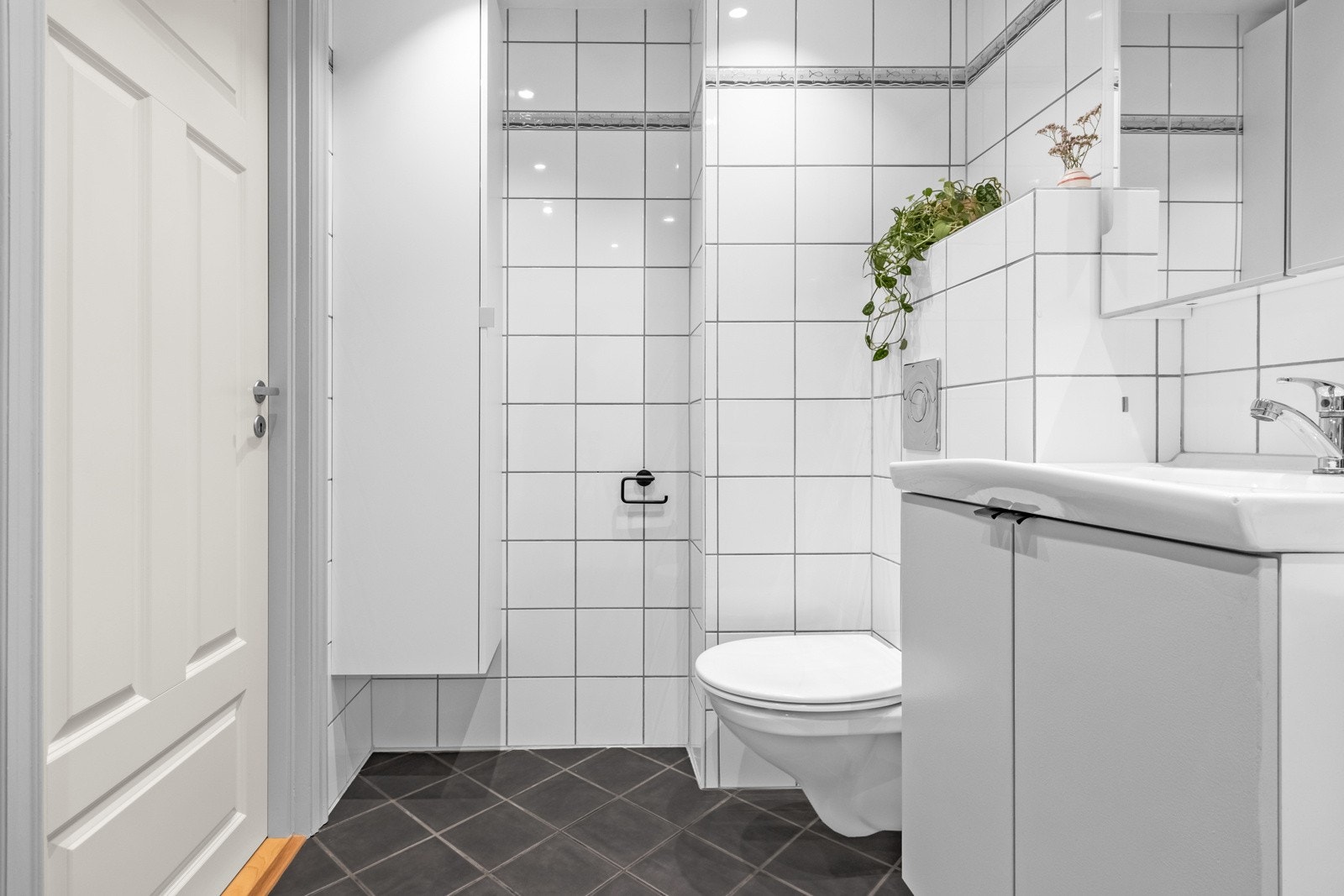 Videre er badet utstyrt med veggmontert toalett, nedfelt servant med underskap og speilskap over servant. Galleribilde