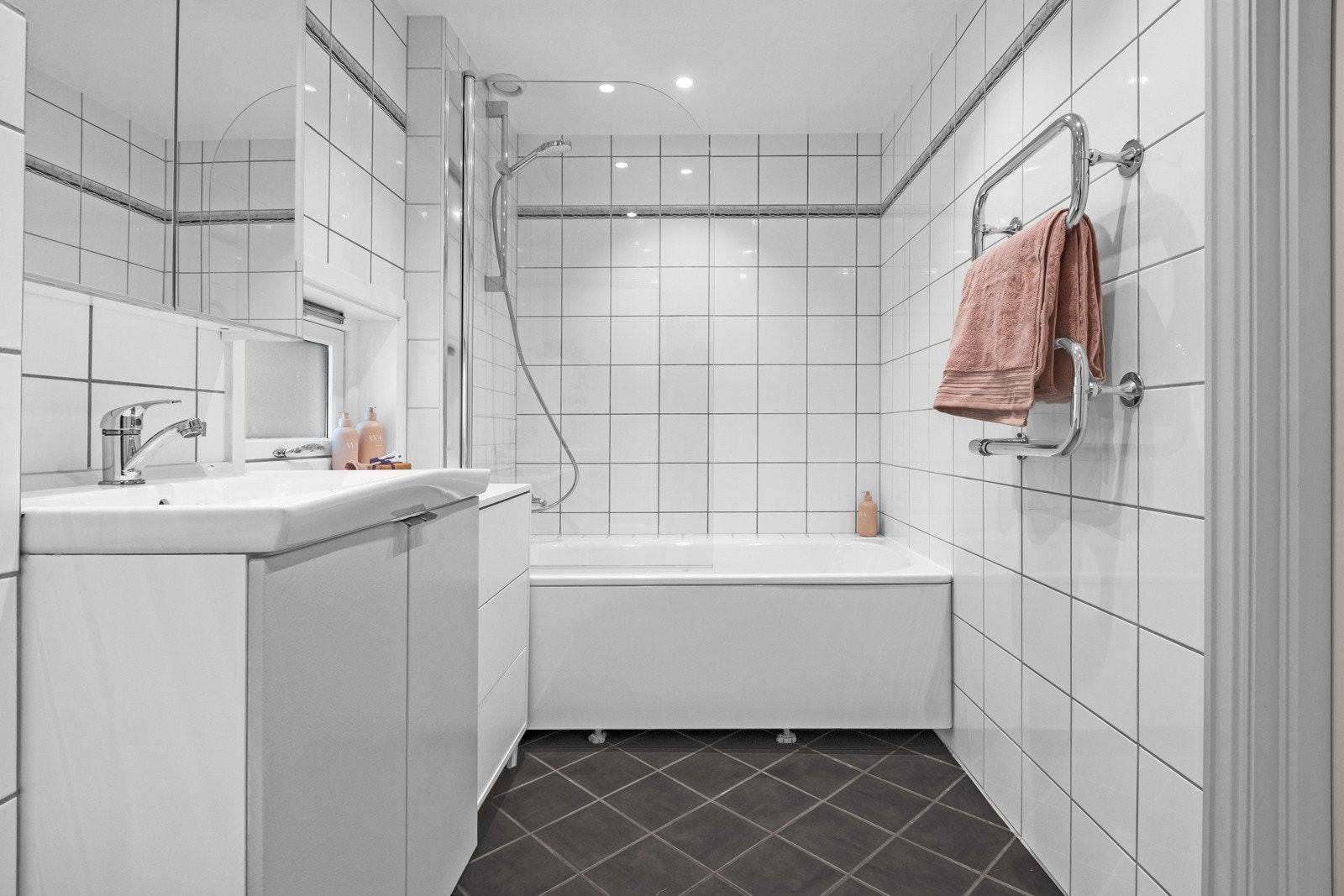 Romslig og pent flislagt baderommed varmekabler i gulv. Badet har et funksjonelt badekar med innfellbar glassdører som gir flere valgmuligheter for hele familien. Galleribilde