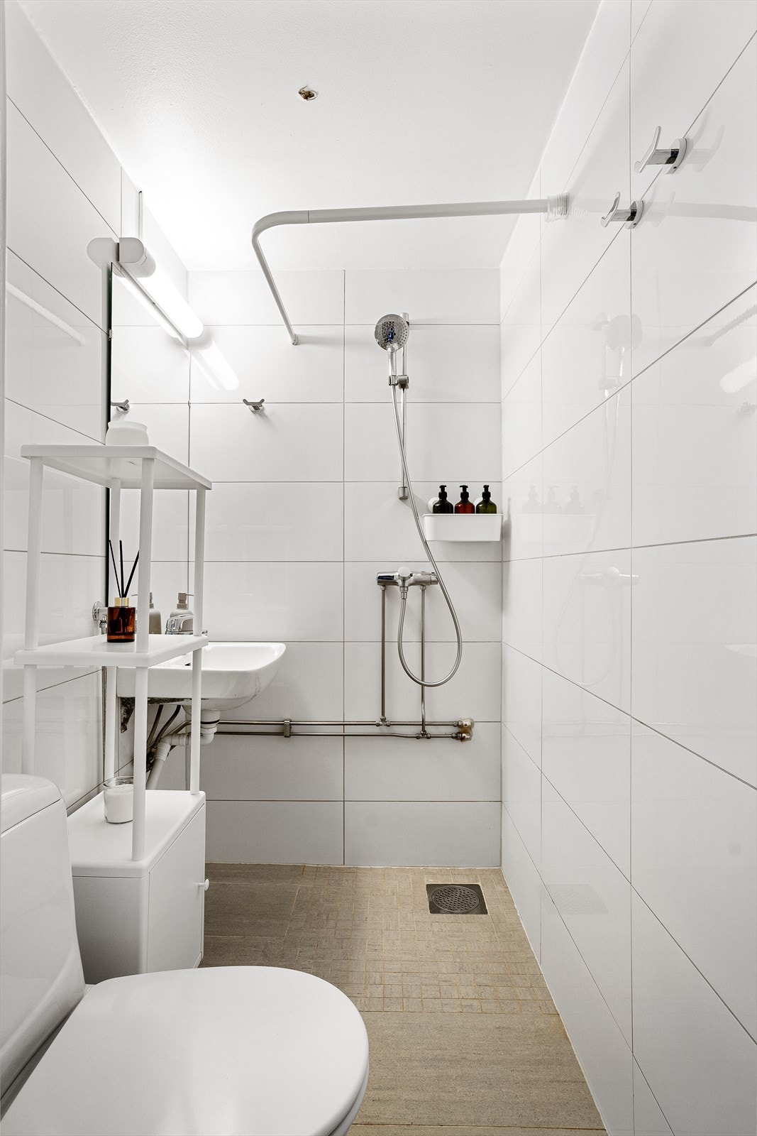 Badet er utstyrt med vegghengt servant med ett-greps armatur, vegghengt speil med overbelysning og gulvstående toalett. Videre er det dusjhjørne med forheng og dusjarmatur tilkoblet hånddusj. Galleribilde