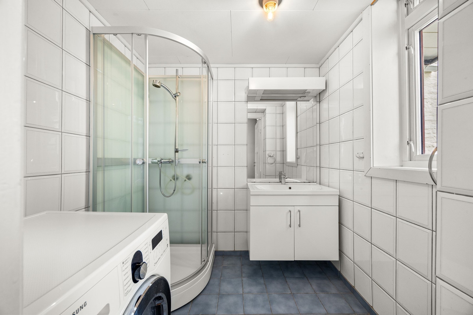 Badet er innredet med dusjkabinett, vegghengt skap med servant, speil med overlys, samt opplegg og plass for vaskemaskin. Galleribilde