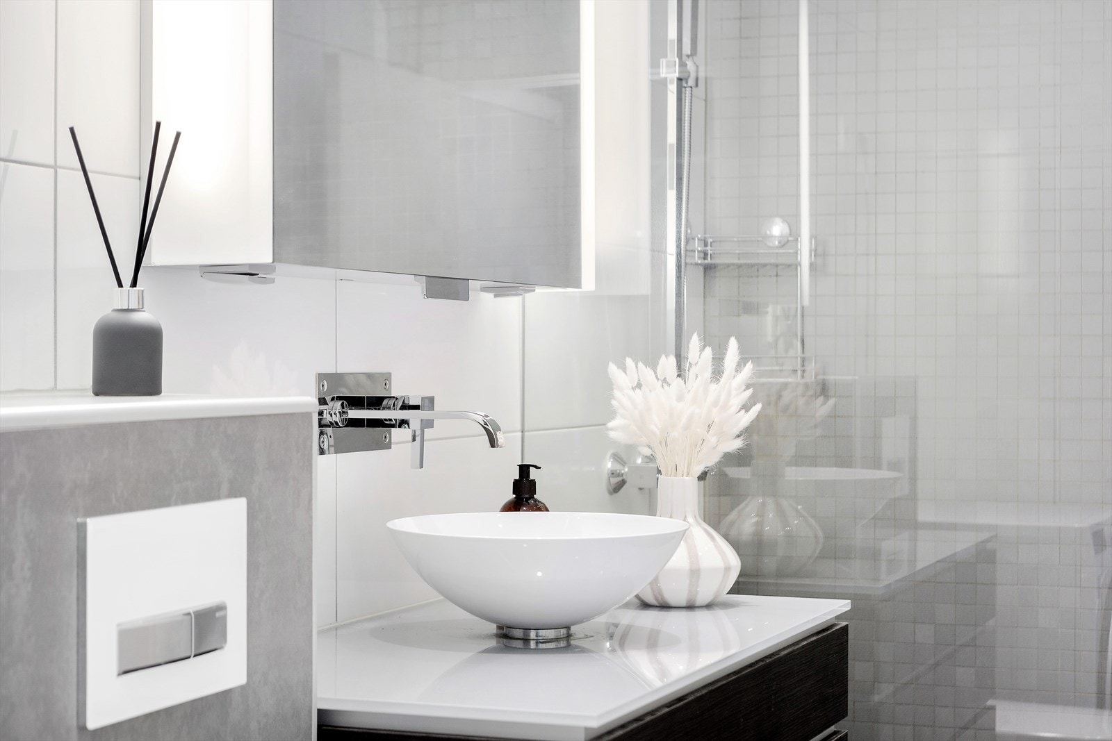 Badet er utstyrt med servantskap med slette og finérlaminerte fronter, benkeplate av glass med overmontert hvit servant i stål og vegghengt blandebatteri i rustfritt stål fra Tapwell samt overskap med speilfront Galleribilde
