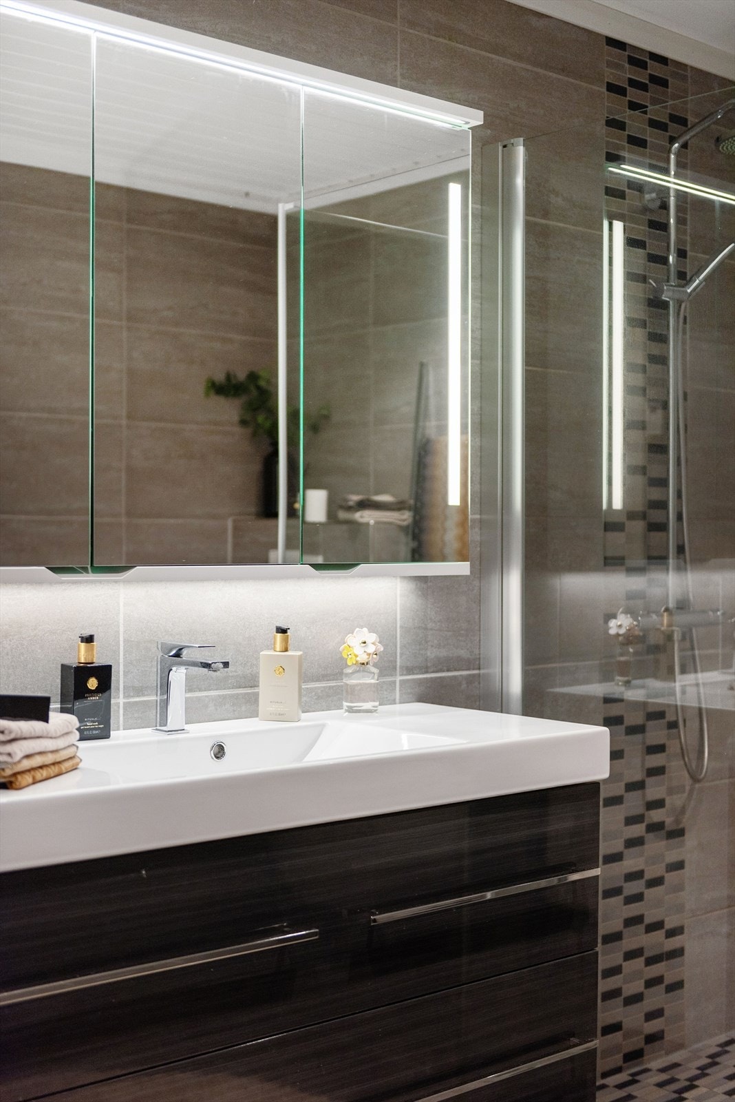 Moderne baderomsinnredning med skuffer og heldekkende servant, vegghengt speilskap med integrert belysning over. Galleribilde