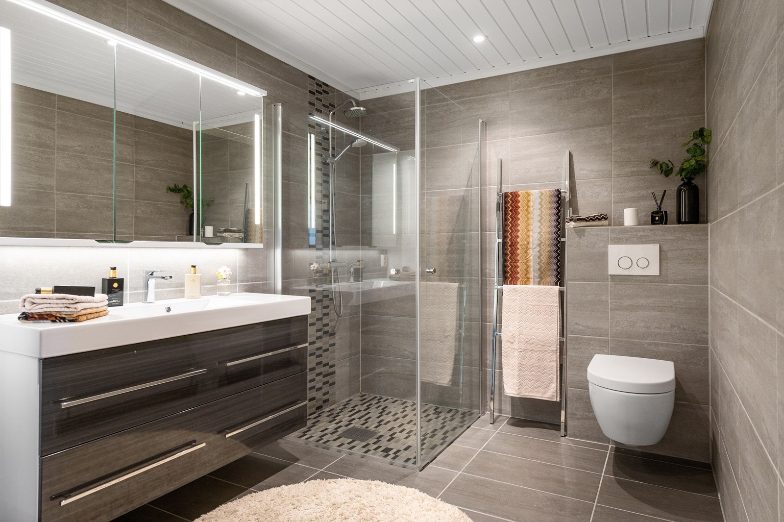 Baderommet er også utstyrt med romslig dusjhjørne med innfellbare glassdører og både hånd- og regnfallsdusj, samt vegghengt toalett. Galleribilde