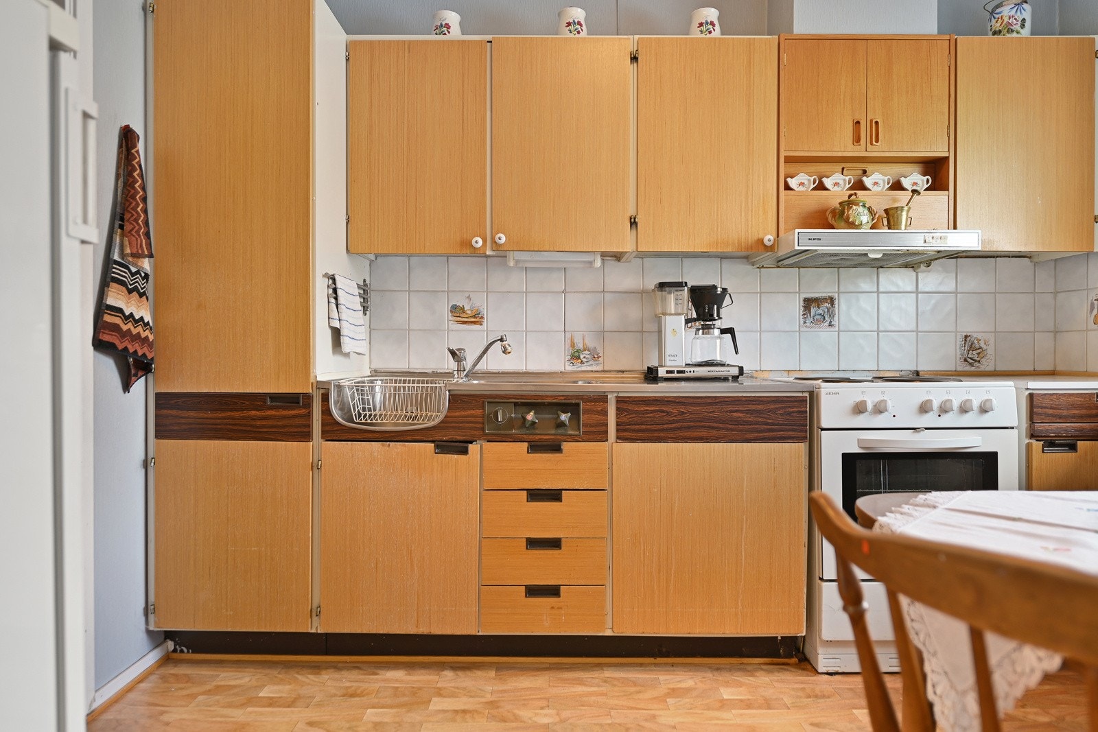 Kjøkkenet på 7 kvm er originalt fra byggeåret og trenger oppgradering. Her finner du en enkel kjøkkeninnredning med hvite slette fronter og en laminert benkeplate. Galleribilde