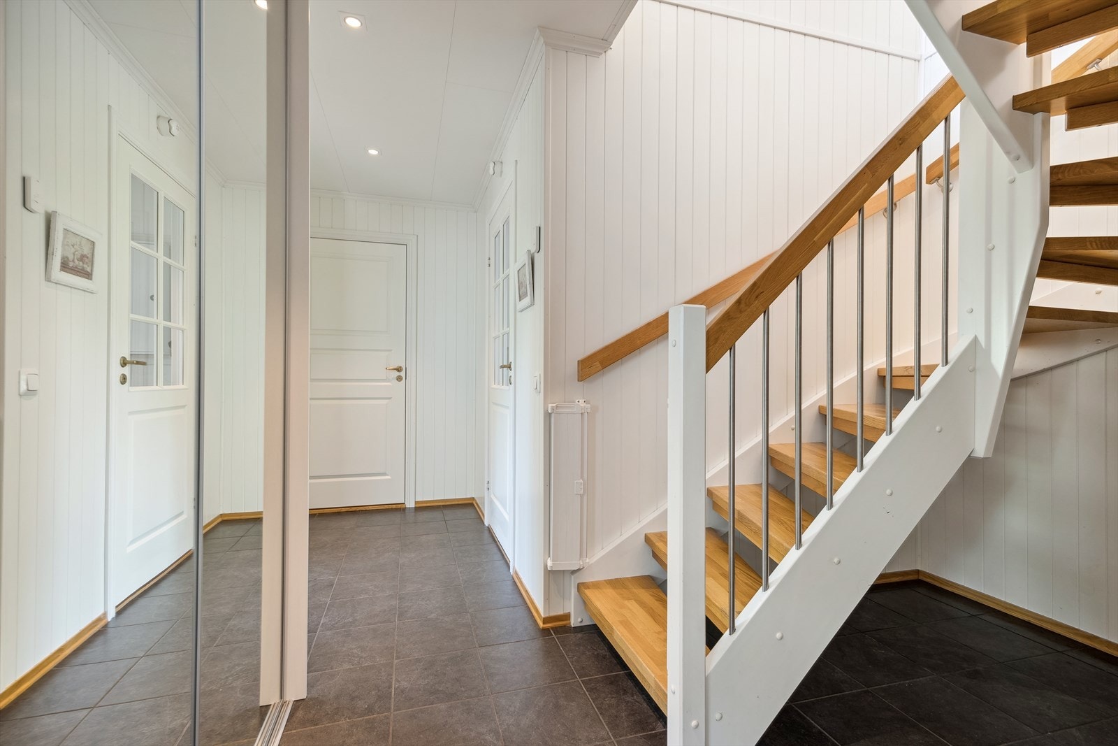 Entreen har fliser på gulv med gulvvarme og vegger med panel - en stil som strekker seg videre inn i trappegangen. Galleribilde
