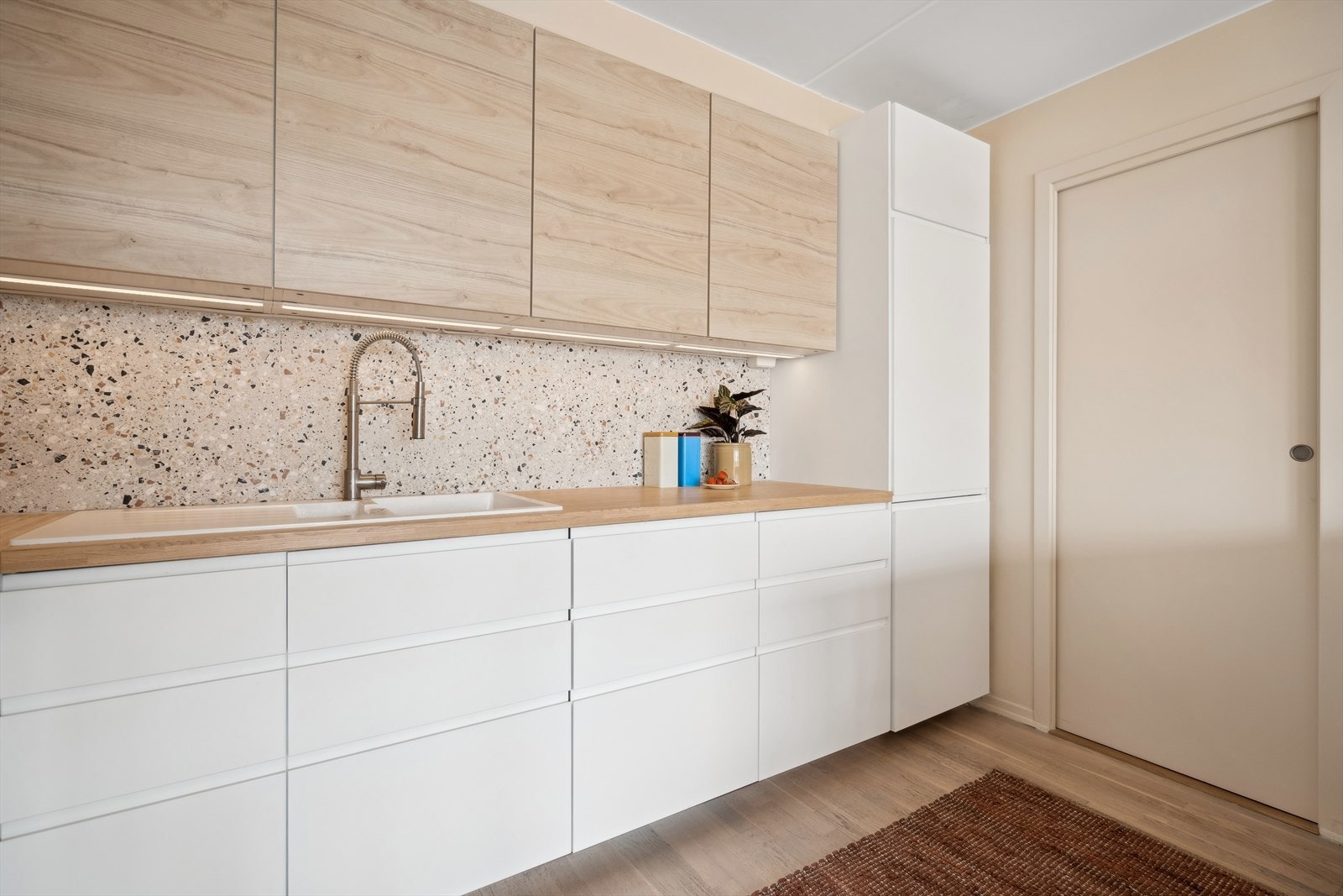 Kjøkkeninnredningen har mye skap- og benkeplass og består av stilrene fronter i en myk tone, lekre fliser og en pen benkeplate. Galleribilde