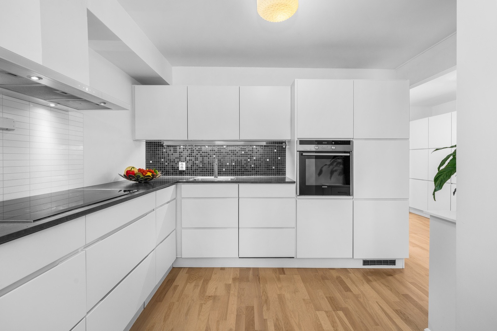 Kjøkkenet fremstår som både klassisk og tidsriktig med en innredning bestående av hvite, glatte fronter med tilhørende svart laminat benkeplate med tilhørende mørke fliser over, som sammen skaper en herlig kontrast. Galleribilde