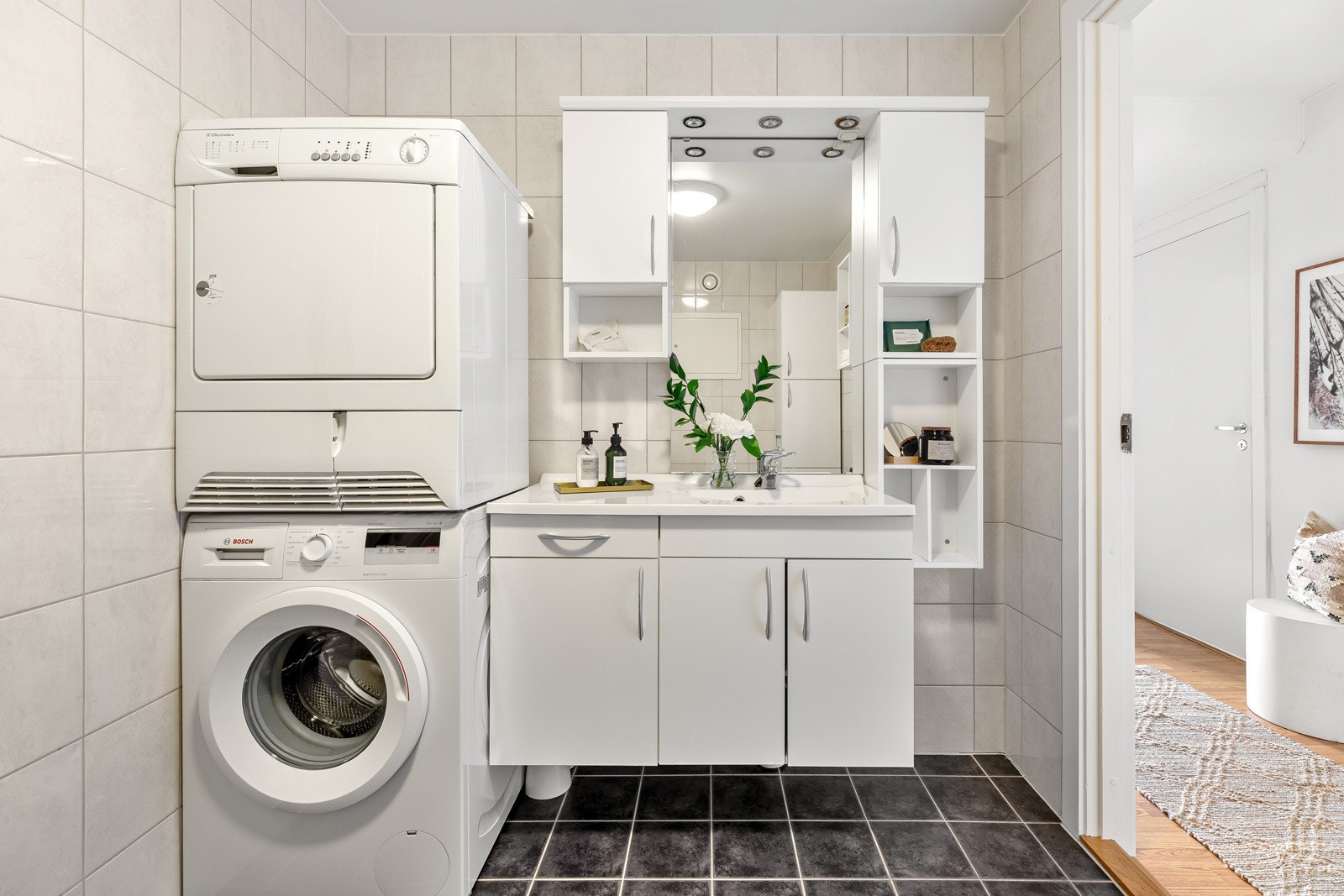Badet er av praktisk størrelse med plass til dusjhjørne, veggmontert servantinnredning og gulvstående klosett samt vaskemaskin og tørketrommel Galleribilde