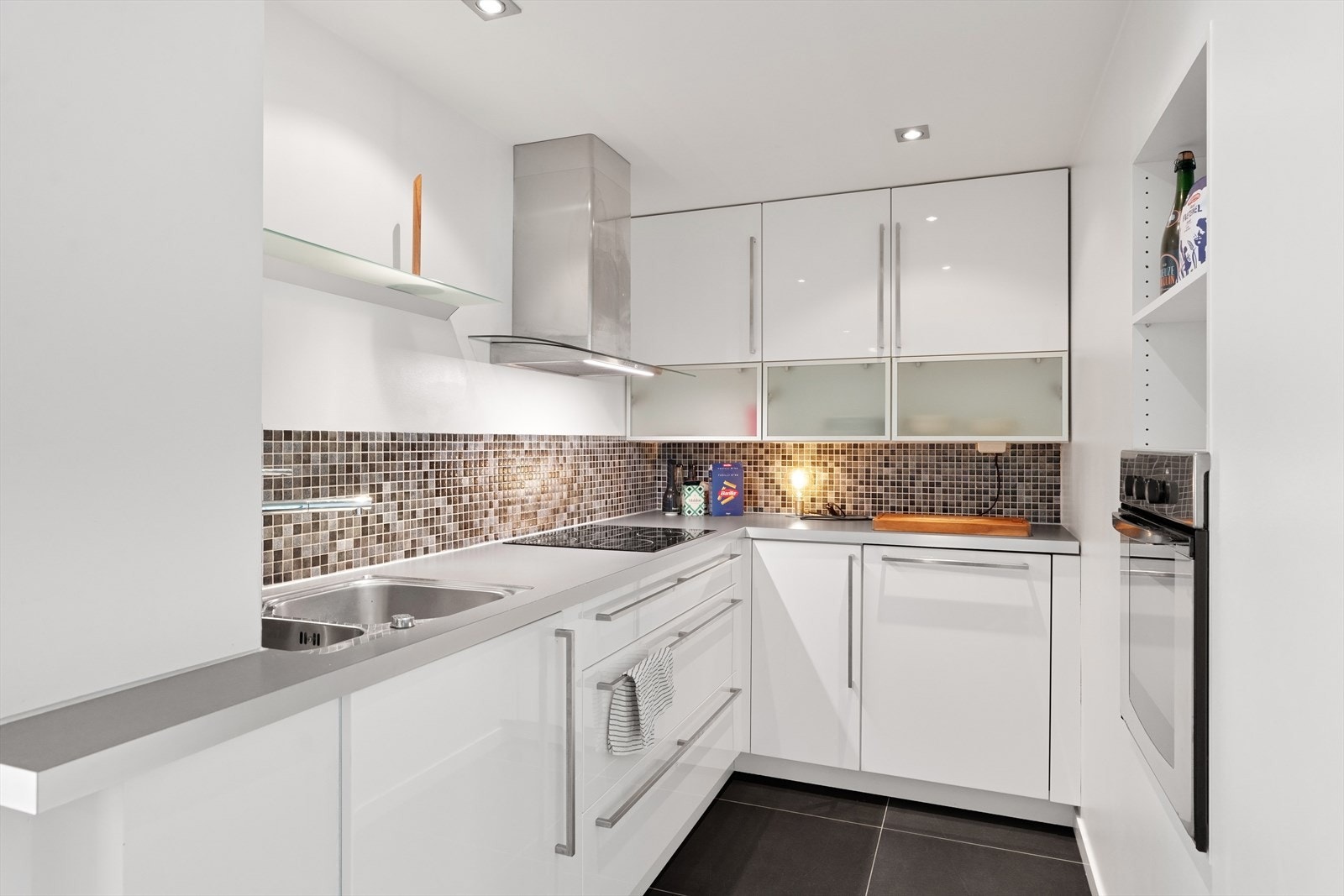 Lyst og stilrent Ikea laminat høyglans kjøkkeninnredning. Kjøkkenet er utstyrt med integrert komfyr, plateopp og oppvaskmaskin, samt ventilator med kullfilter. Galleribilde