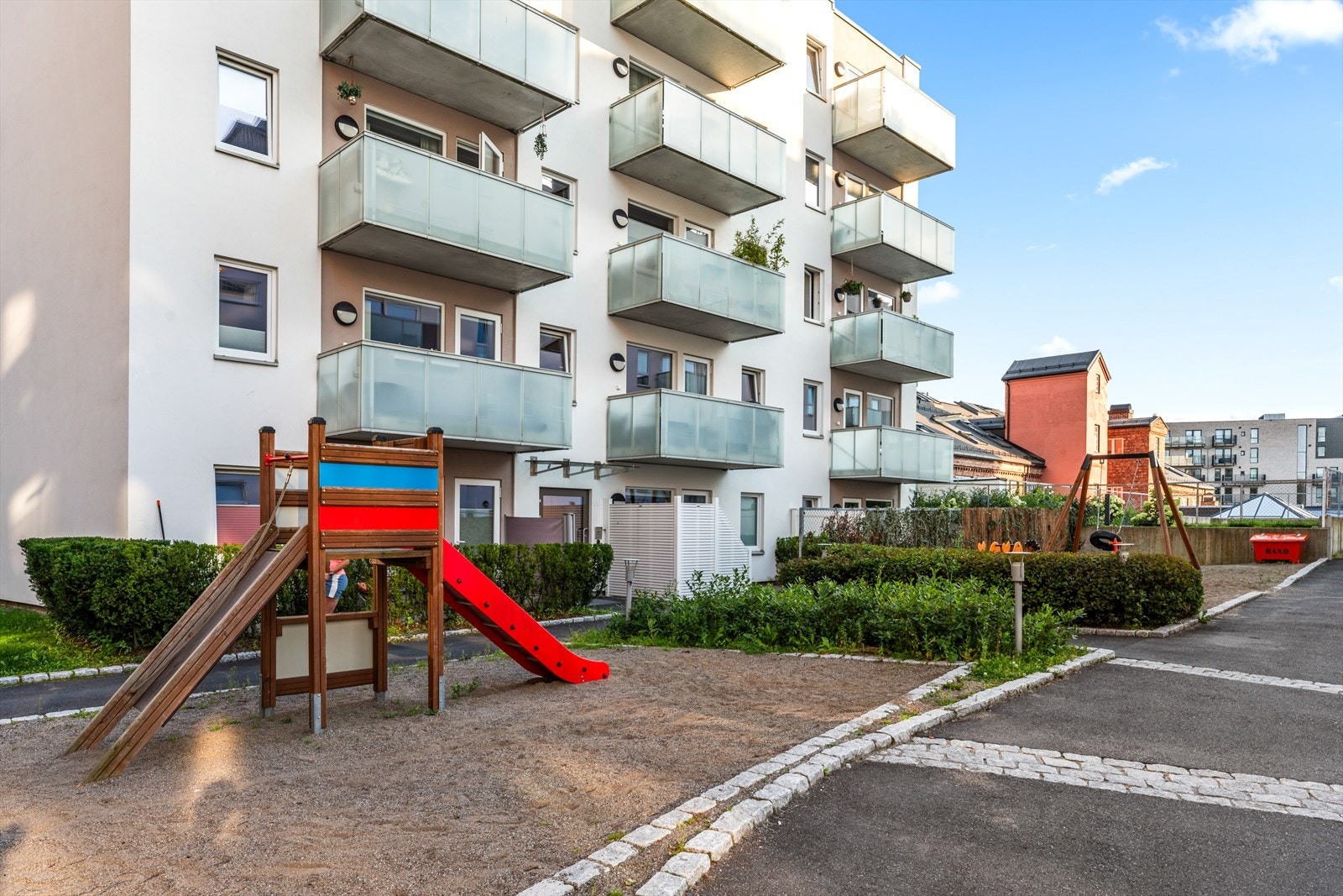 Pent opparbeidet bakgård med lekeapparater, beplantning og asfaltert adkomst. Galleribilde