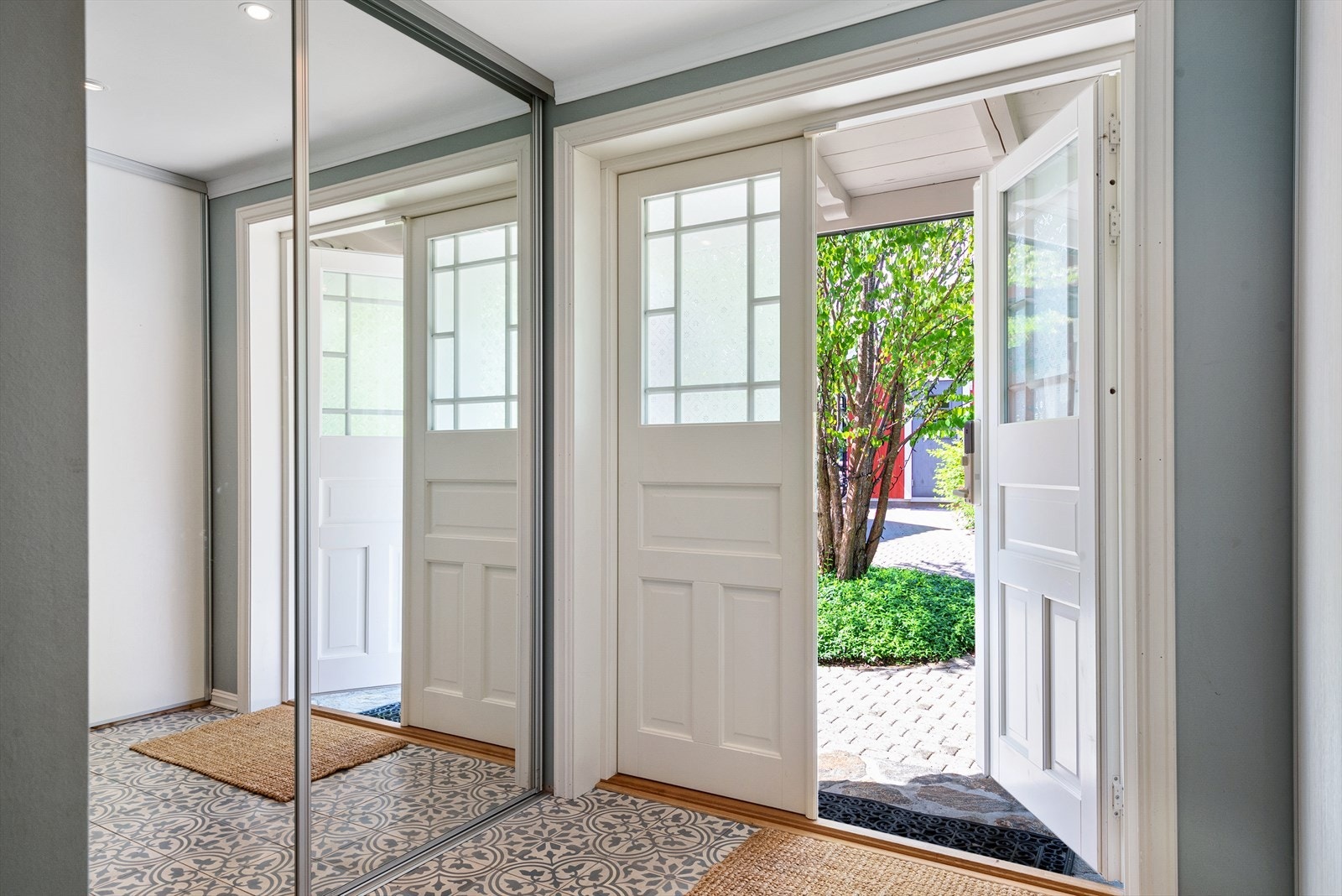 Vel inne er en romslig entré med klassiske mønsterfliser på gulv og godt med oppbevaringsplass i skyvedørsgarderober med speildører. Galleribilde