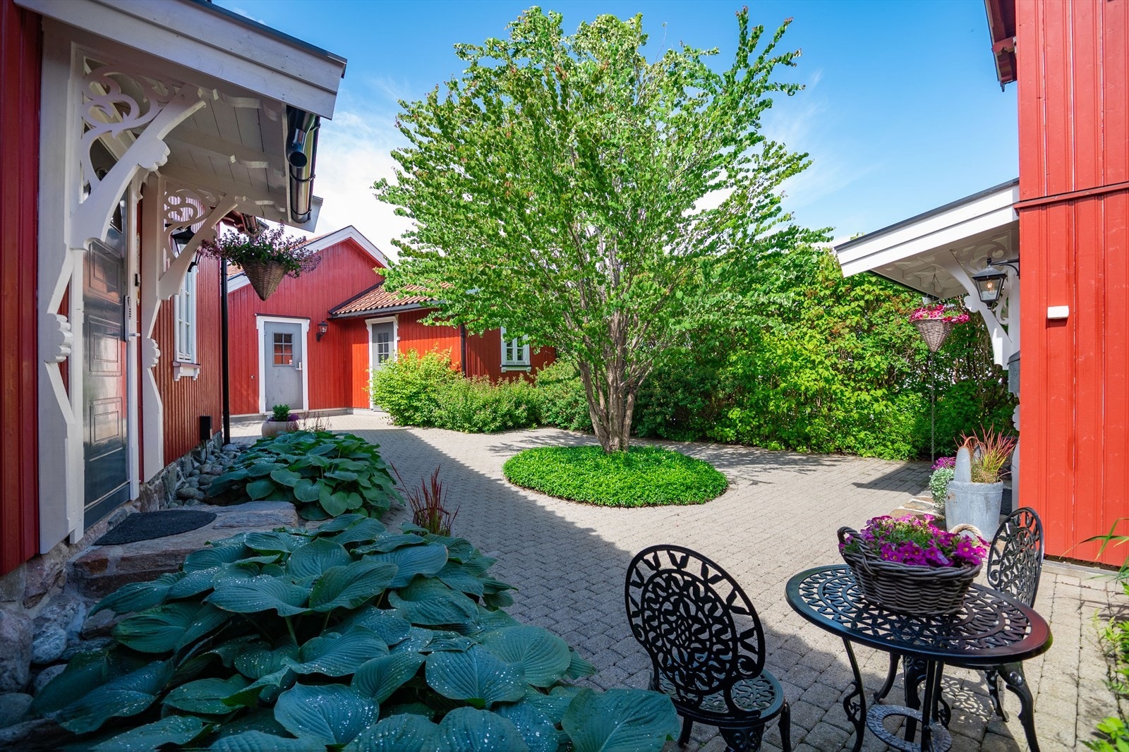 Innenfor gjerdet og porten møtes man av en flott gårdsplass med belegningsstein og et grønt midtplassert tre omgitt av variert beplantning. Galleribilde