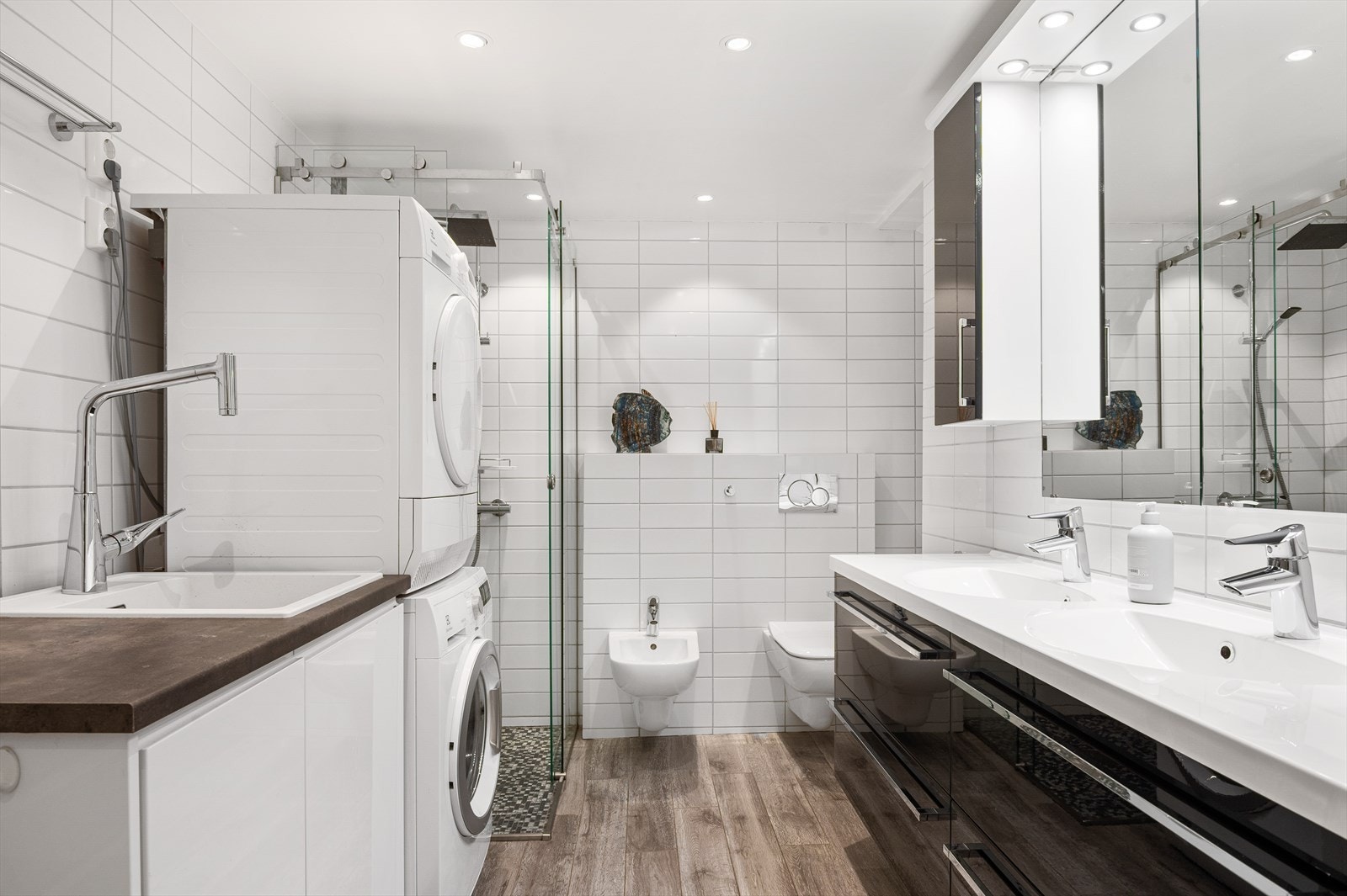 Bad/vaskerommet i anneks er fra ca. 2014 og har et lyst og tidløst uttrykk med flislagte overflater. Rommet har dusjnisje med skyvedør i glass, regnfallsdusj og mosaikkflis, vegghengt toalett og bidet. Galleribilde