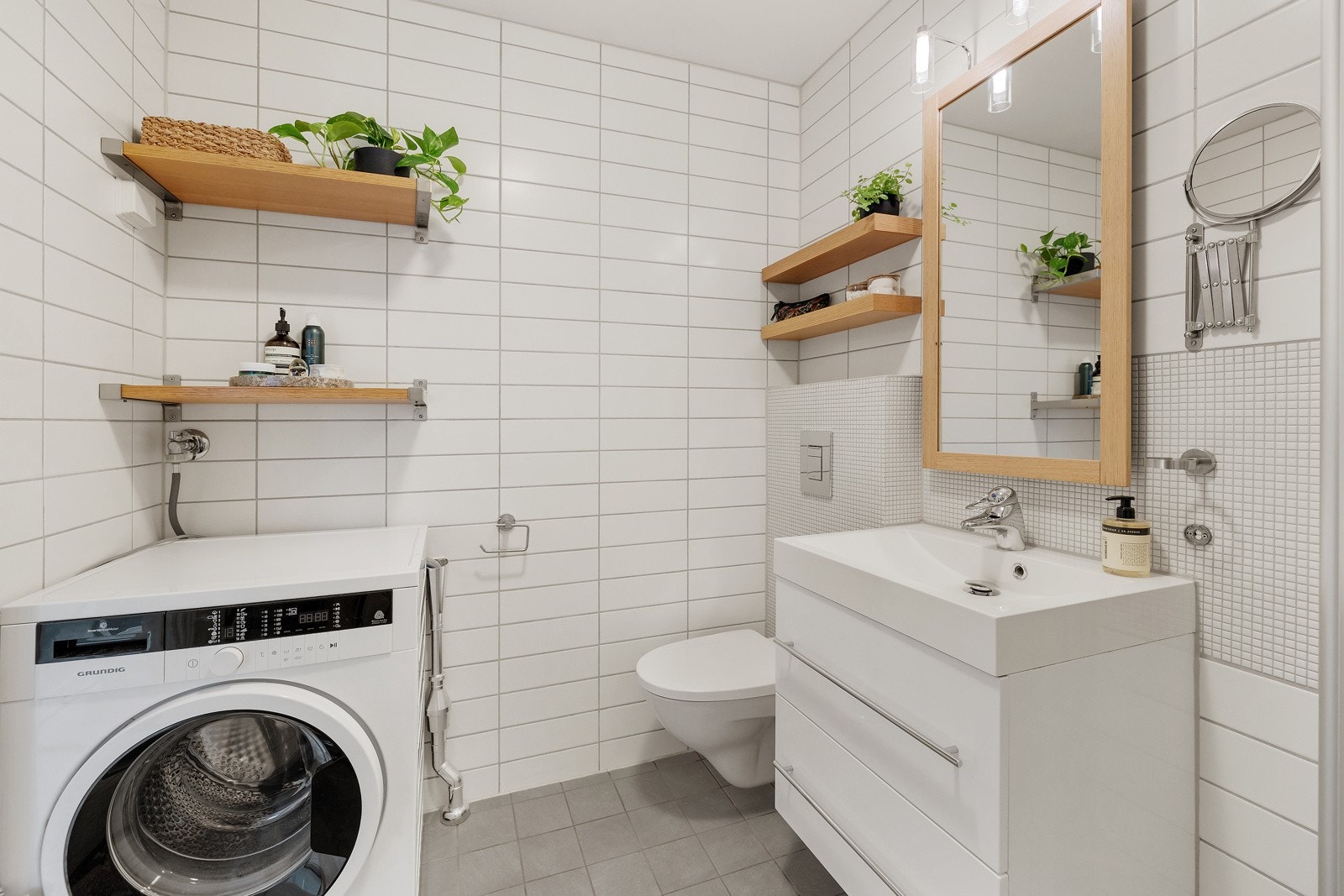 Badet inneholder vegghengt servantskap med heldekkende servant, vegghengt speil med overbelysning, vegghengt wc og dusjhjørne med innfellbare dører. Galleribilde