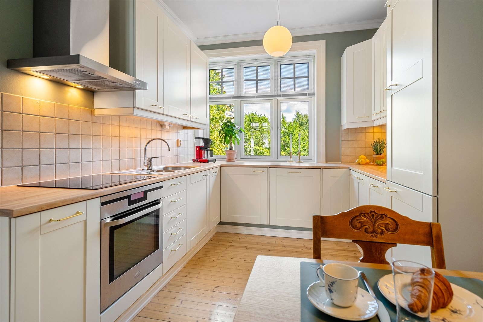 Pent, separat kjøkken med spiseplass. Tidløst kjøkken med lyse, profilerte fronter med nyere håndtak og fliser på vegg over kjøkkenbenk Galleribilde