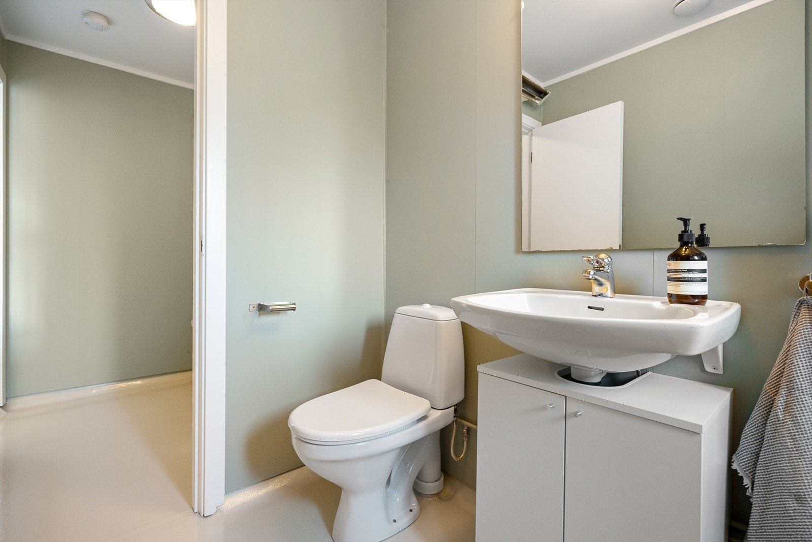 Badet er utstyrt med dusjkabinett, mekanisk avtrekk, gulvmontert toalett og servantskap med servant og blandebatteri fra FM Mattsson Galleribilde