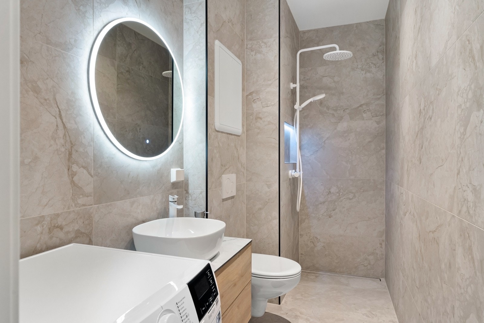 Lekkert og delikat baderom som består av dusjhjørne, vegghengt toalett, servant over innredning og speil med lys. Galleribilde