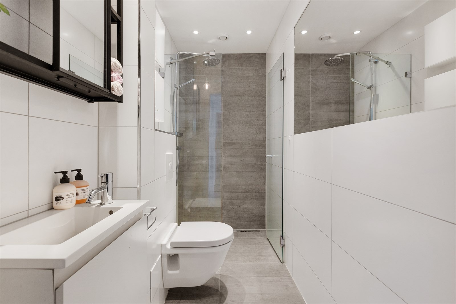 Flislag bad innredet med smakfulle, minimalistiske detaljer. Dusjhjørne, vegghengt toalett og praktiske oppbevaringsløsninger. Galleribilde