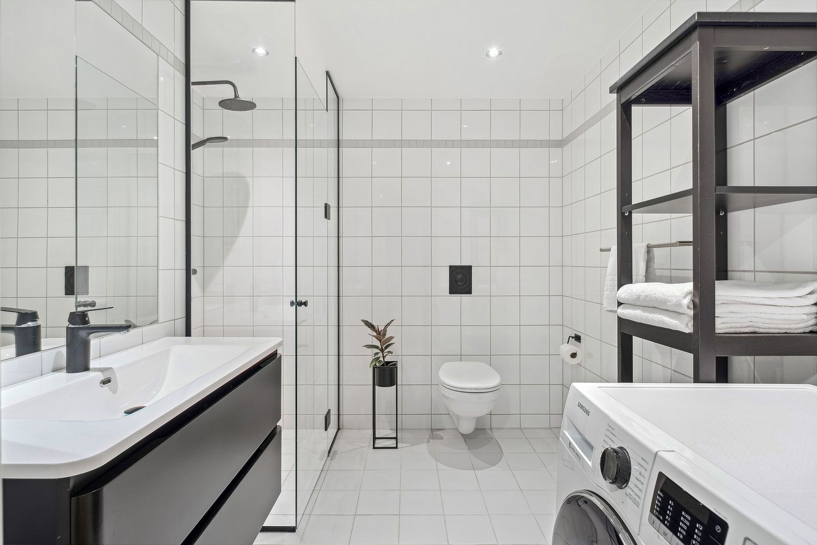 Helfliset baderom med enkel servant, dusjnisje, vegghengt toalett og opplegg for vaskemaskin. Galleribilde