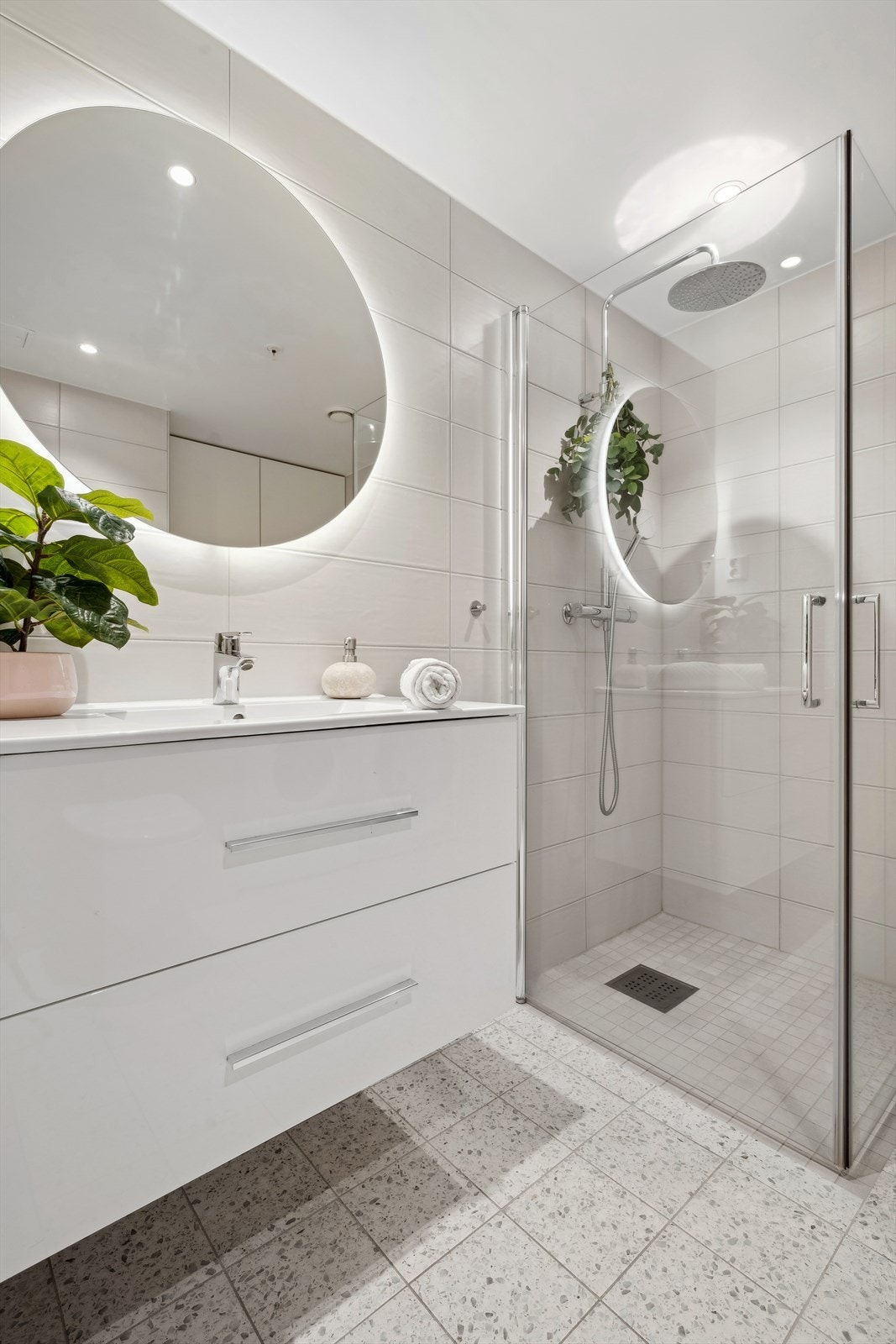 Badet er innredet med dusjhjørne med svingbare glassdører, vegghengt klosett, servant med skuffeseksjon som gir god plass til oppbevaring av baderomsartikler. Galleribilde