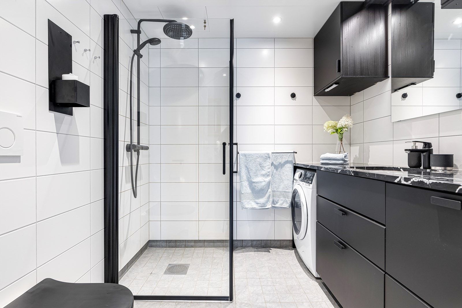 Badet er nøytralt flislagt med hvite fliser på vegg og grå på gulv. På dette badet er det godt med skapplass, og opplegg for vaskemaskin. Varmekabler i gulv. Galleribilde