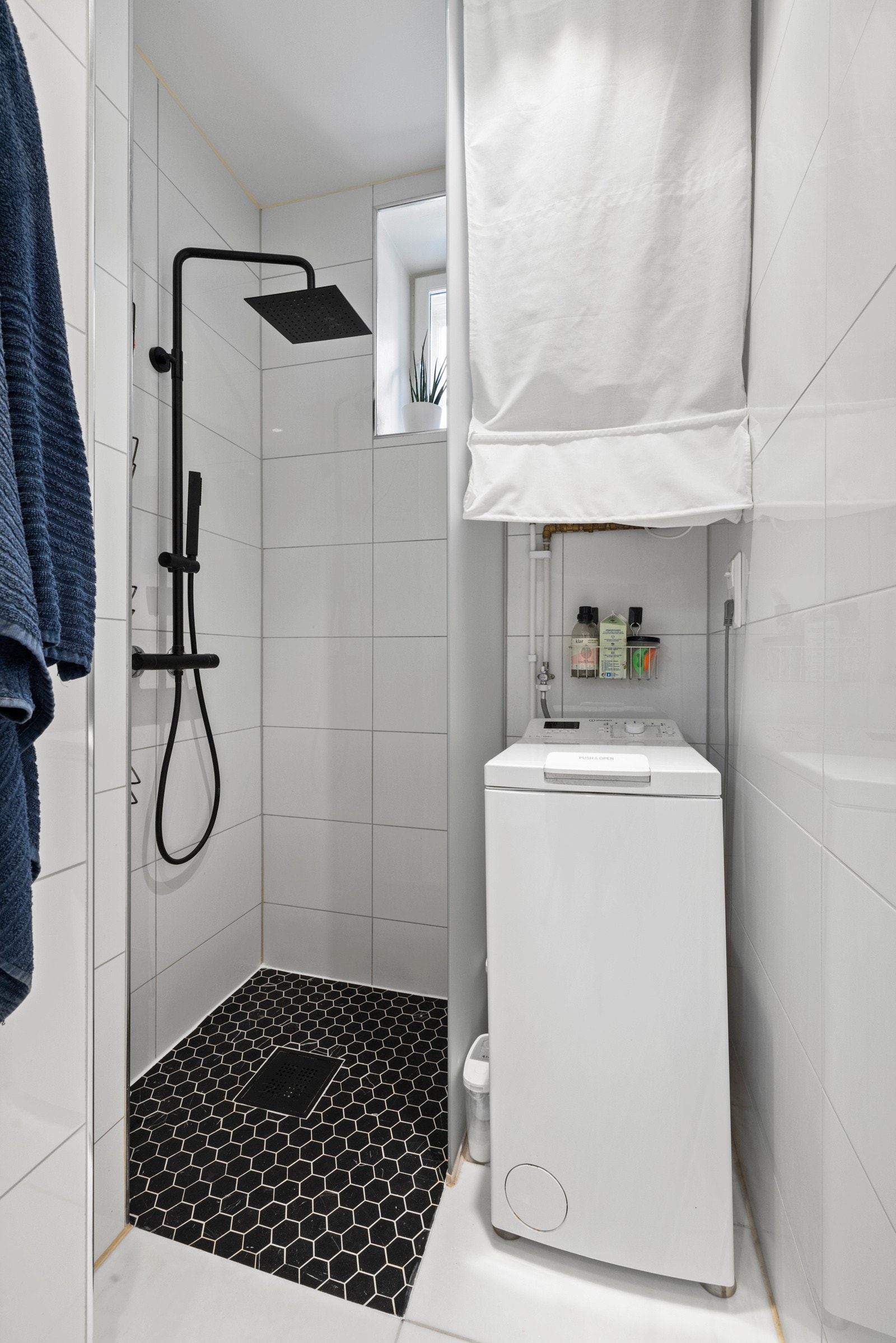 Badet er utstyrt med veggmontert toalett, dusjnisje med både sort håndgarnityr og regnfallsdusj, samt opplegg for vaskemaskin av smal type Galleribilde