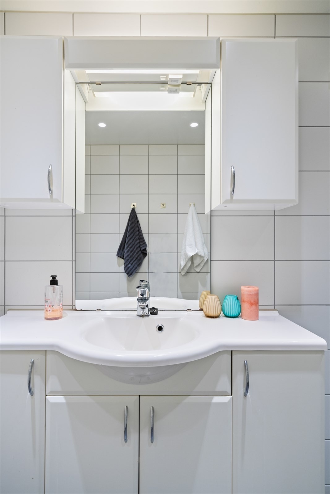 Innredningen på badet består av veggmonterte dusjdører, servant med underskap, speil med lys, overskap samt opplegg for vaskemaskin. Galleribilde