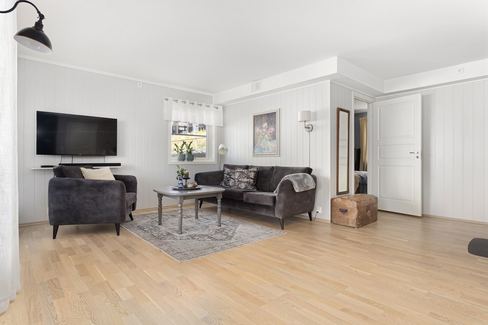 Stuen har overflater malt i lyse fargetoner og eikeparkett på gulv. Galleribilde