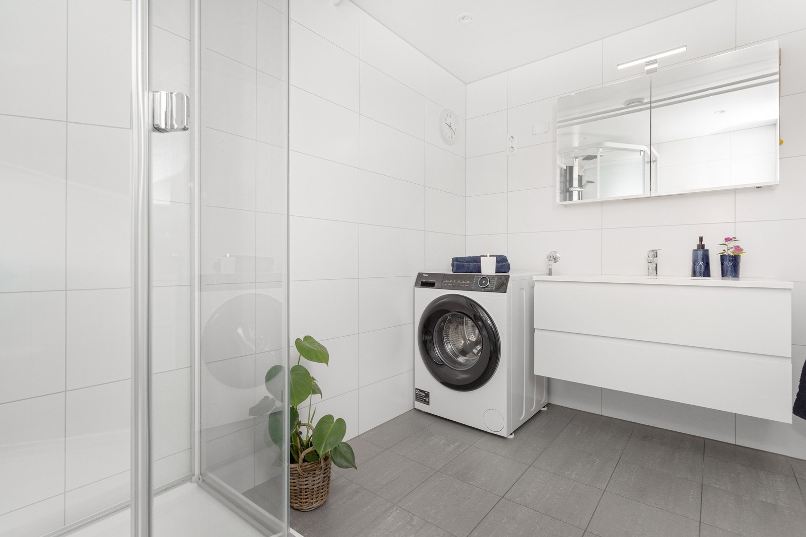 Badet er innredet med servant på skuffeseksjon, dusjkabinett, toalett og har opplegg til vaskemaskin og tørketrommel i søyle. Galleribilde