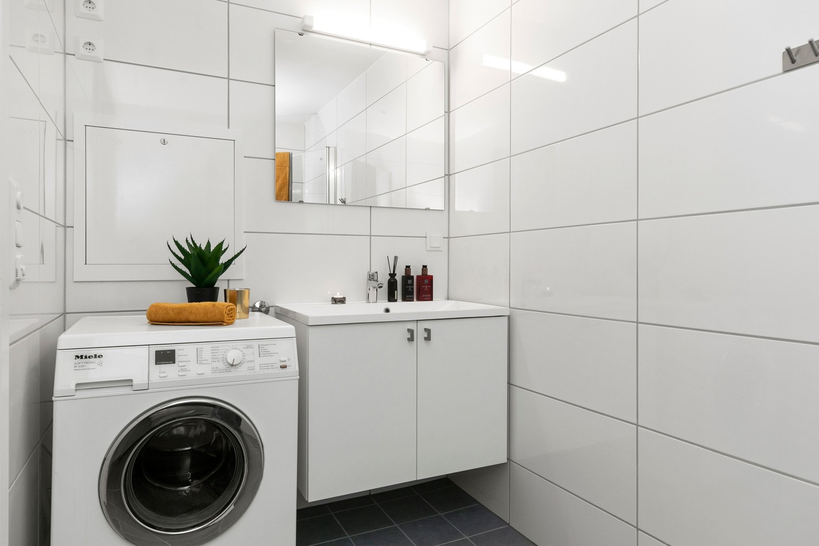 Delikat bad innredet med vask, speil, vegghengt wc og dusj med dusjdører Galleribilde