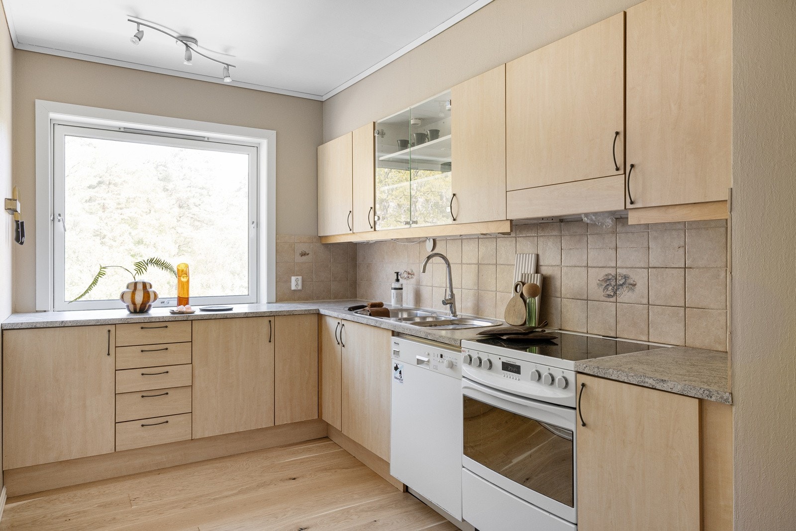 Kjøkkeninnredning med slette fronter, ett glasskap og laminat benkeplate med nedfelt vask av stål. Galleribilde