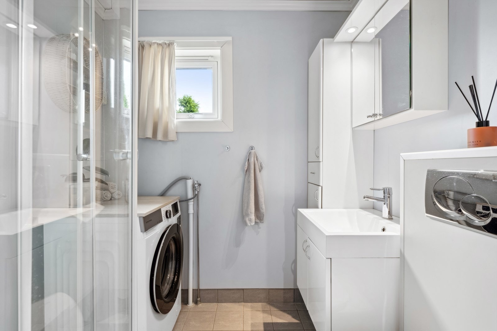 Badet er innredet med vegghengt toalett, opplegg til vaskemaskin, servant med skuffer og speil m/skap og dusjkabinett. Galleribilde