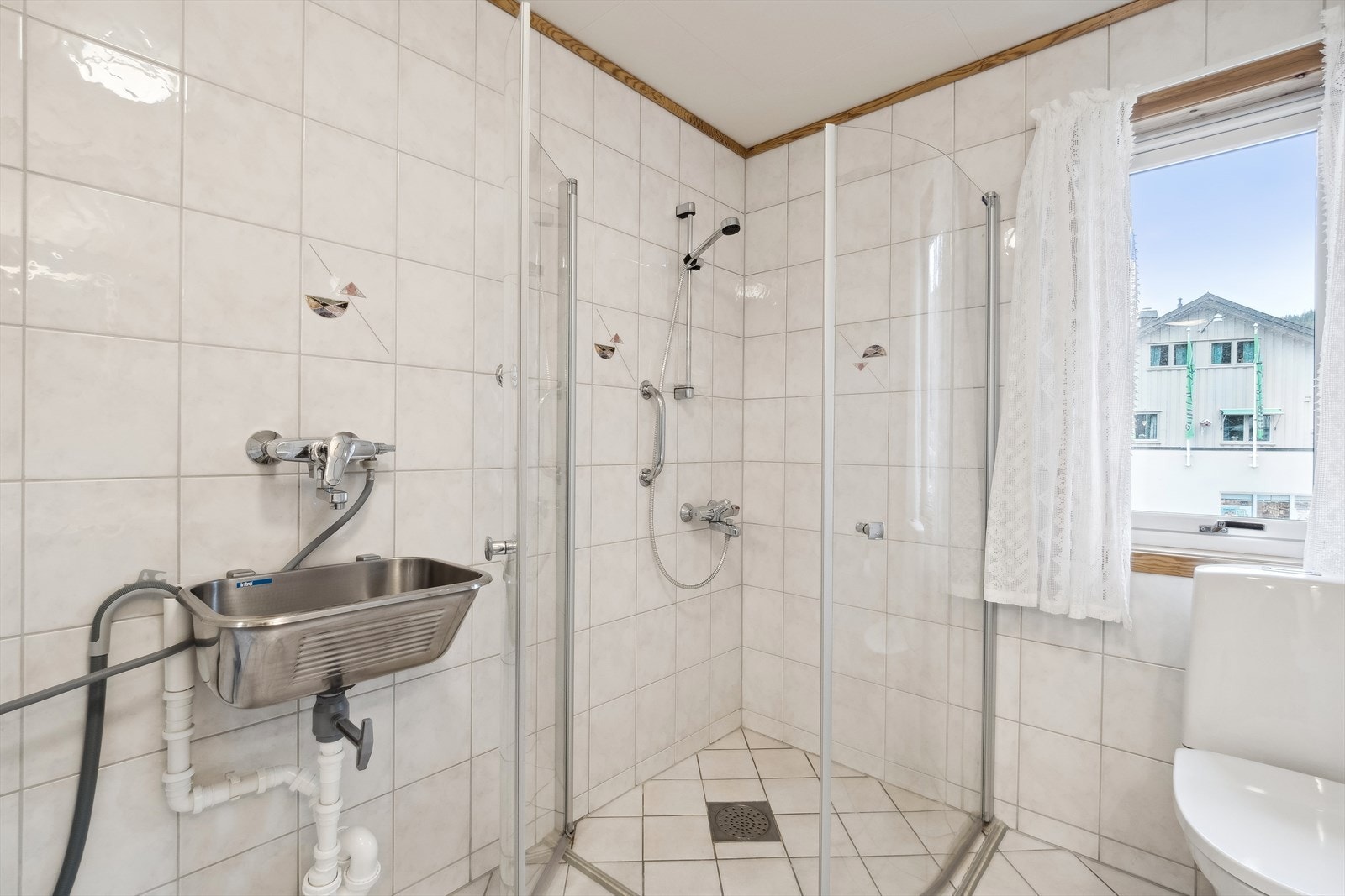 Badet har opplegg for vaskemaskin, buede dusjdører og gulvmontert toalett Galleribilde