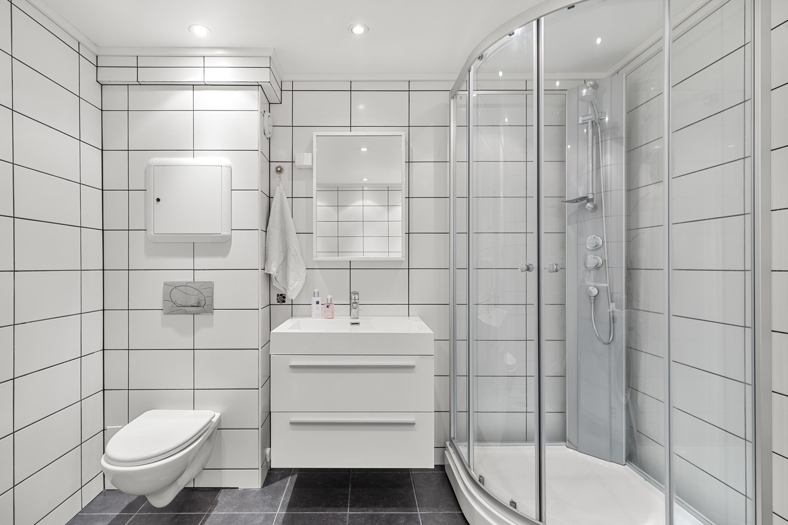 Badet er innredet med nedfelt servant, veggmontert toalett, dusjkabinett og opplegg for vaskemaskin. Galleribilde