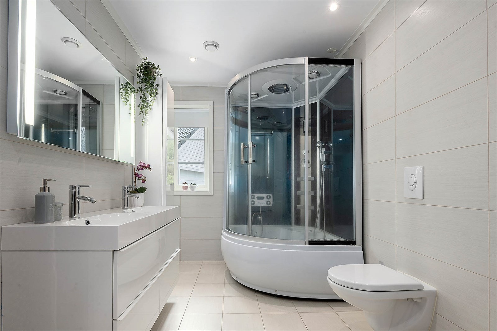 Helfliset bad med downlights i himling og vannbåren varme i gulv. Badet er utstyrt med vegghengt toalett, dusjkabinett og dobbel servant med speil. Galleribilde