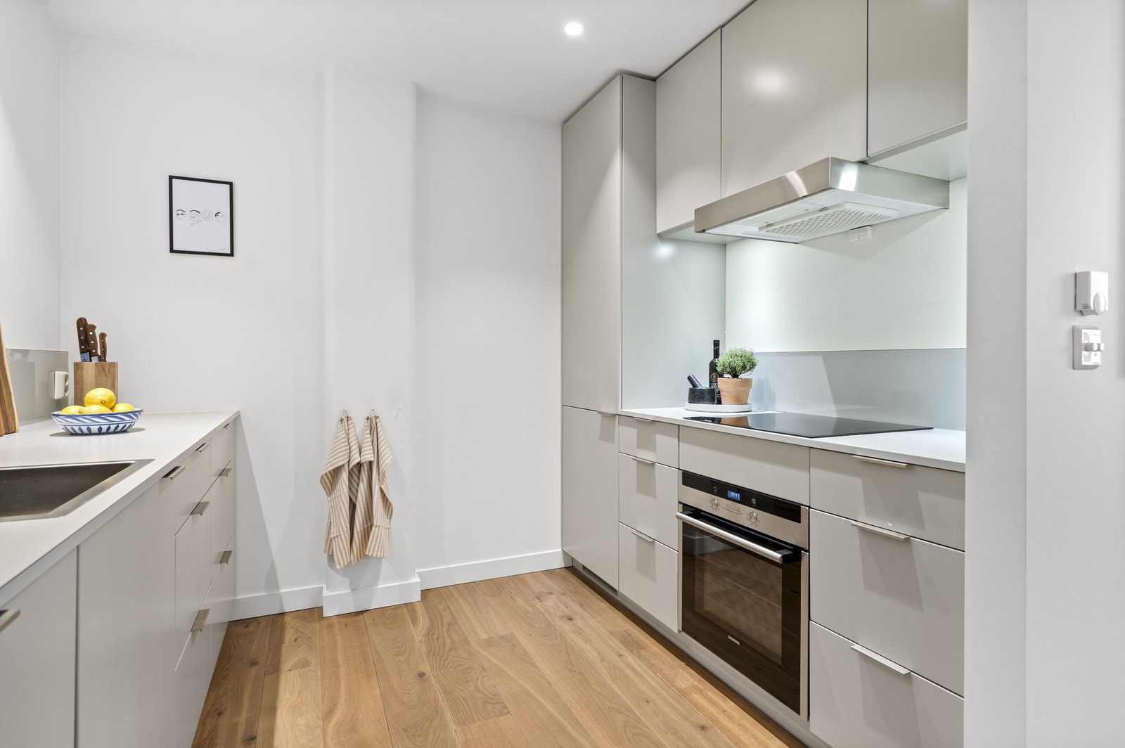 Laminert benkeplate med innfelt kum. Fliser mellom benk og overskap. Det er montert dedikert aquakontroll med panel under kjøkkenbenken samt komfyrvakt over kokeplaten. Galleribilde