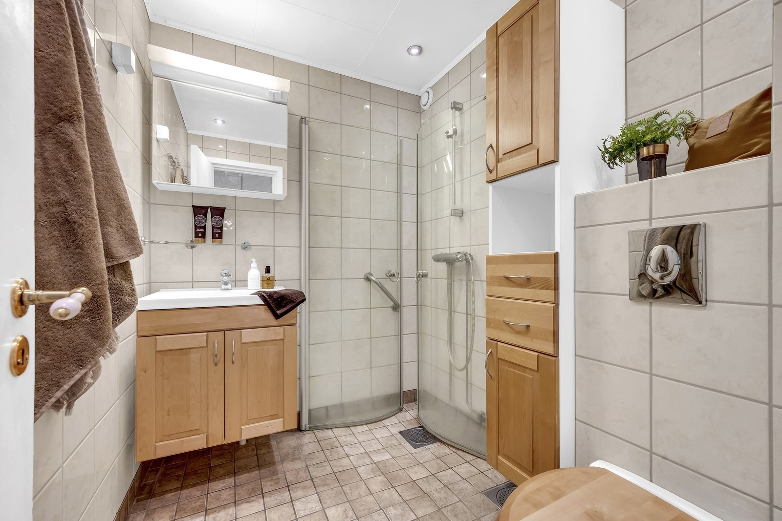 Pent bad med flislagt gulv med gulvvarme, flislagte veggflater, og himlingsflate med takplater og downlights. Galleribilde