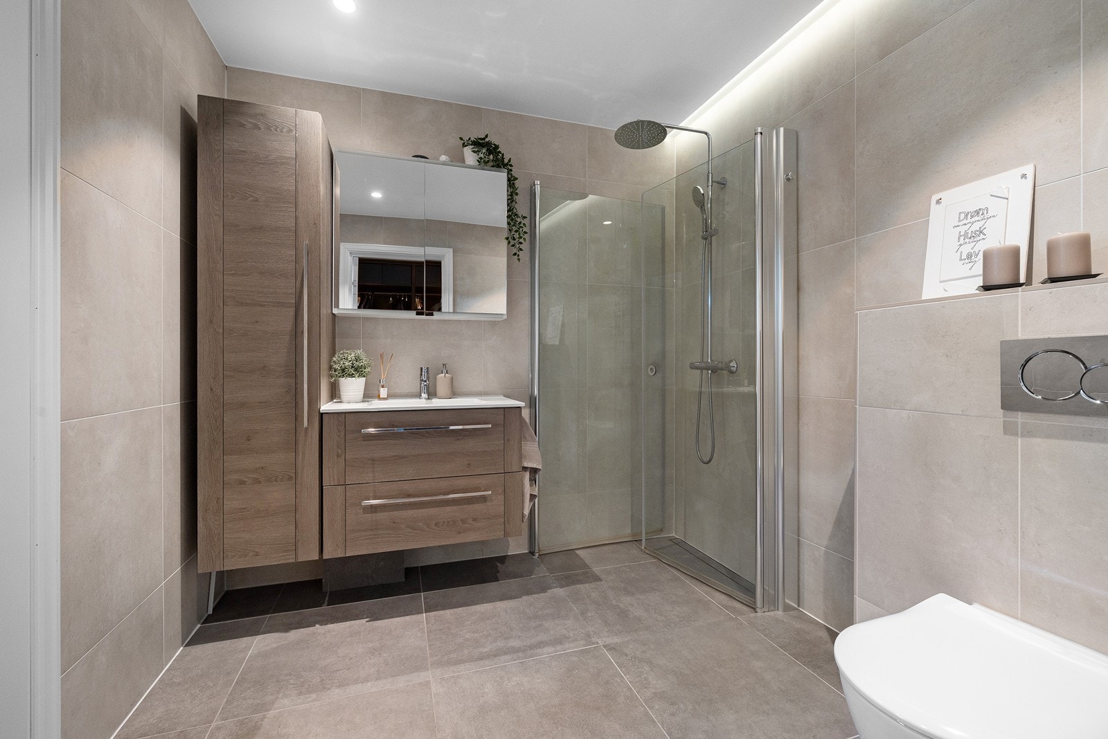 Delikat flislagt bad med varmekabler i gulv. Badet er innredet med vegghengt toalett, servant i baderomsinnredning, vegghengt skap, speilskap og dusjhjørne. Galleribilde