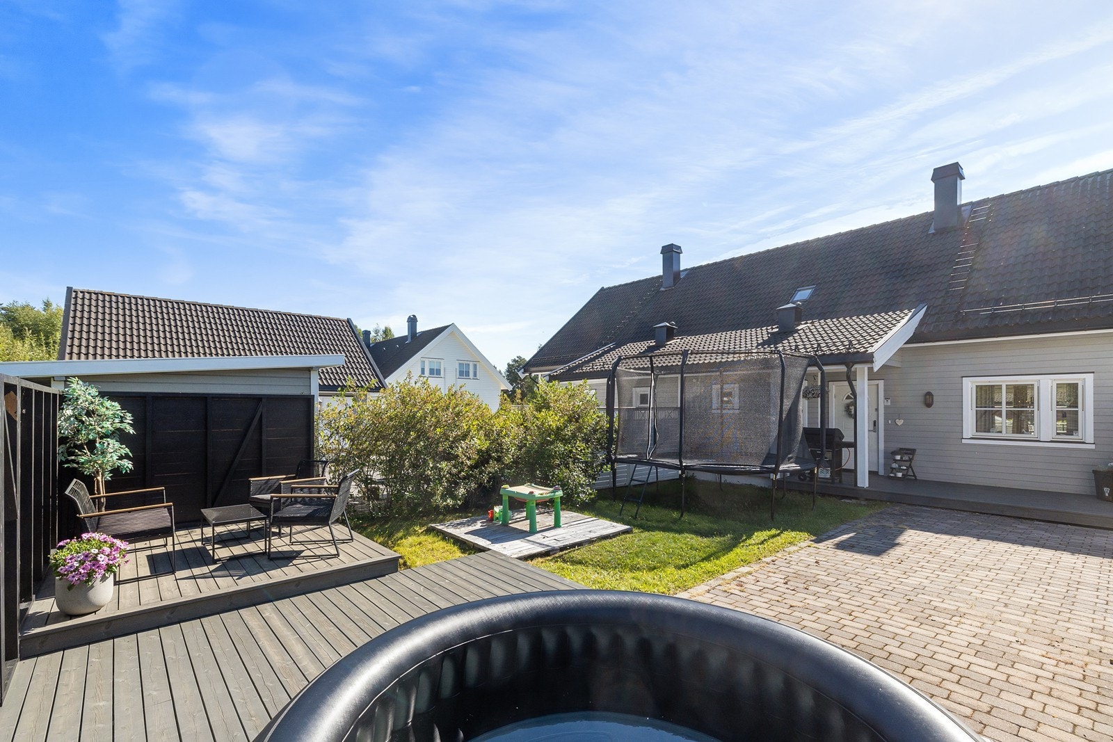 Stor terrasseplatting i bakkant av boligen ved garasjen med levegger, og areal med gressplen. Galleribilde