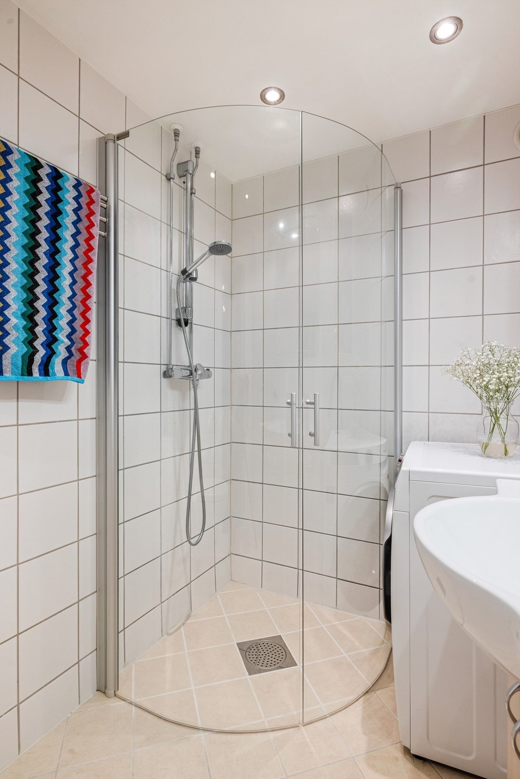 Badet er utstyrt med Dusjhjørne med to svingbare glassdører, slett innredning med heldekkende servant, vegghengt toalett og opplegg for vaskemaskin og tørketrommel. Galleribilde